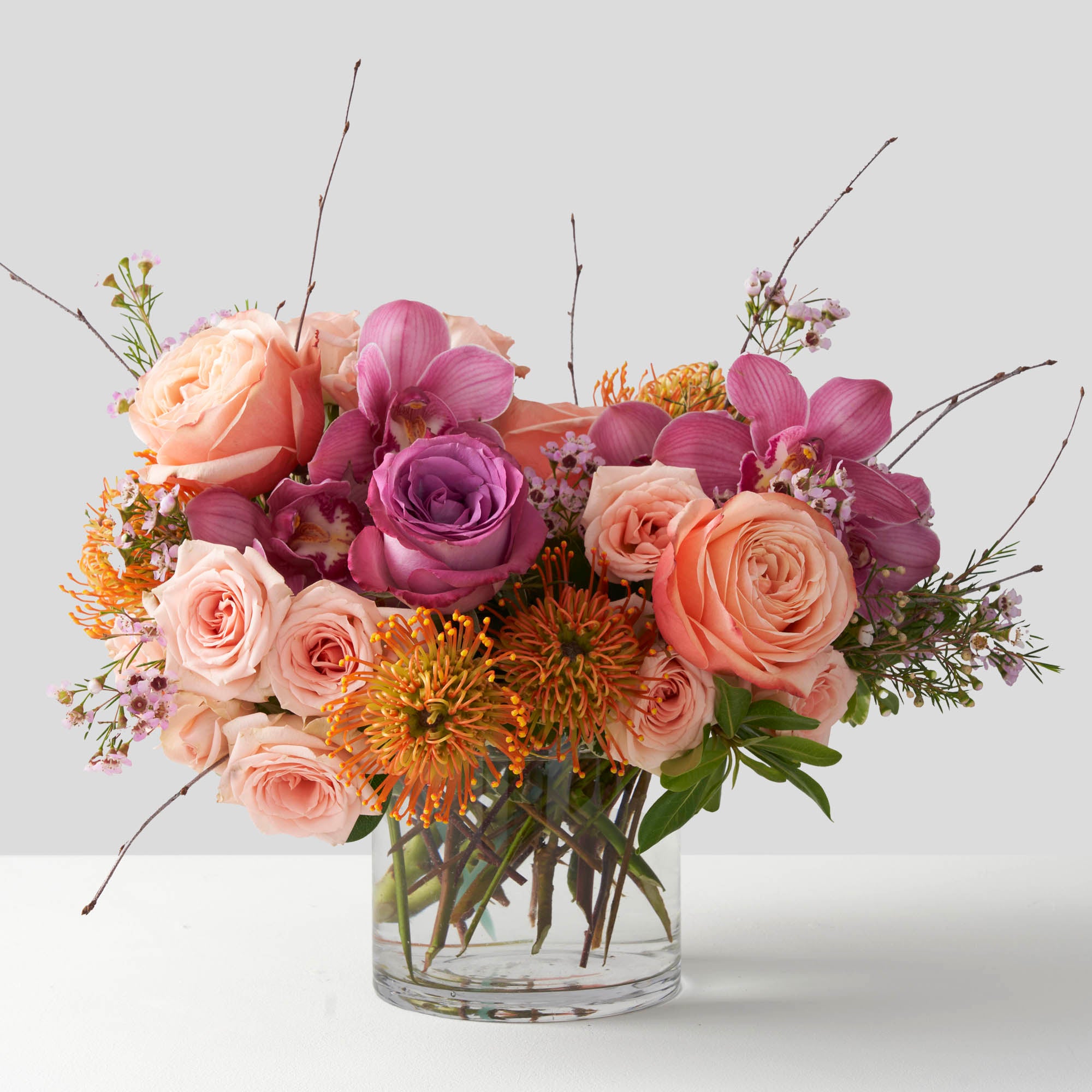 Roses, cybidium orchid, and protea arranged in a glass vase on white background