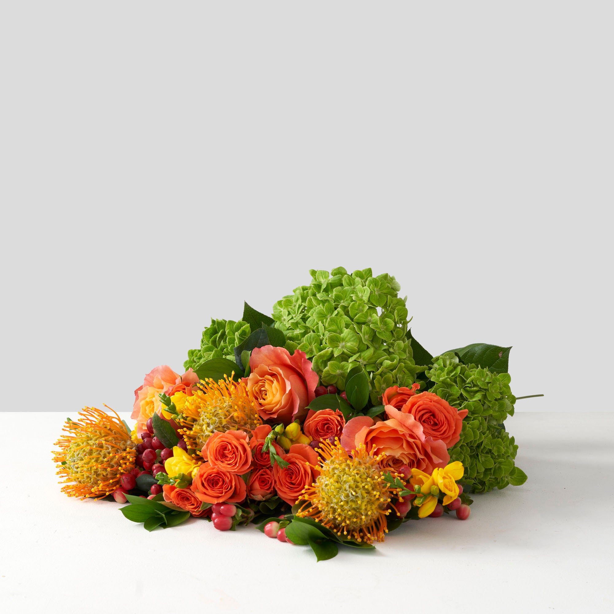 Bouquet of orange, yellow, gold, and green flowers on white background.