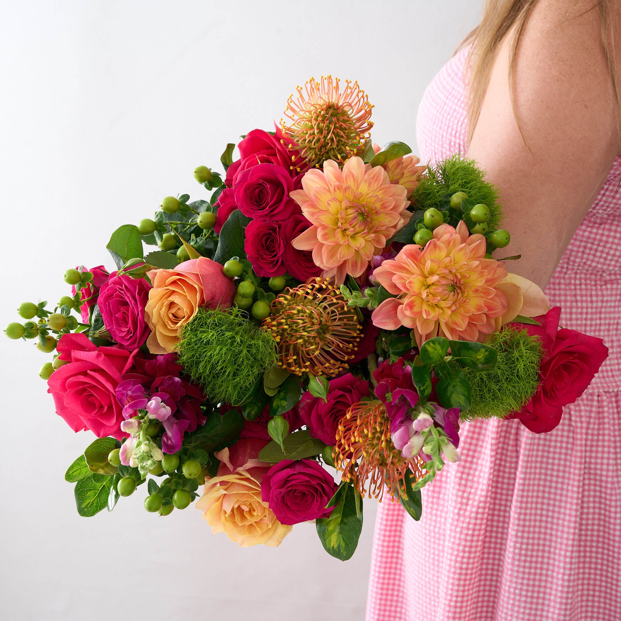 Bouquet of dahlias, green mums, fuchsia and peach roses held by a person wearing a pink dress.