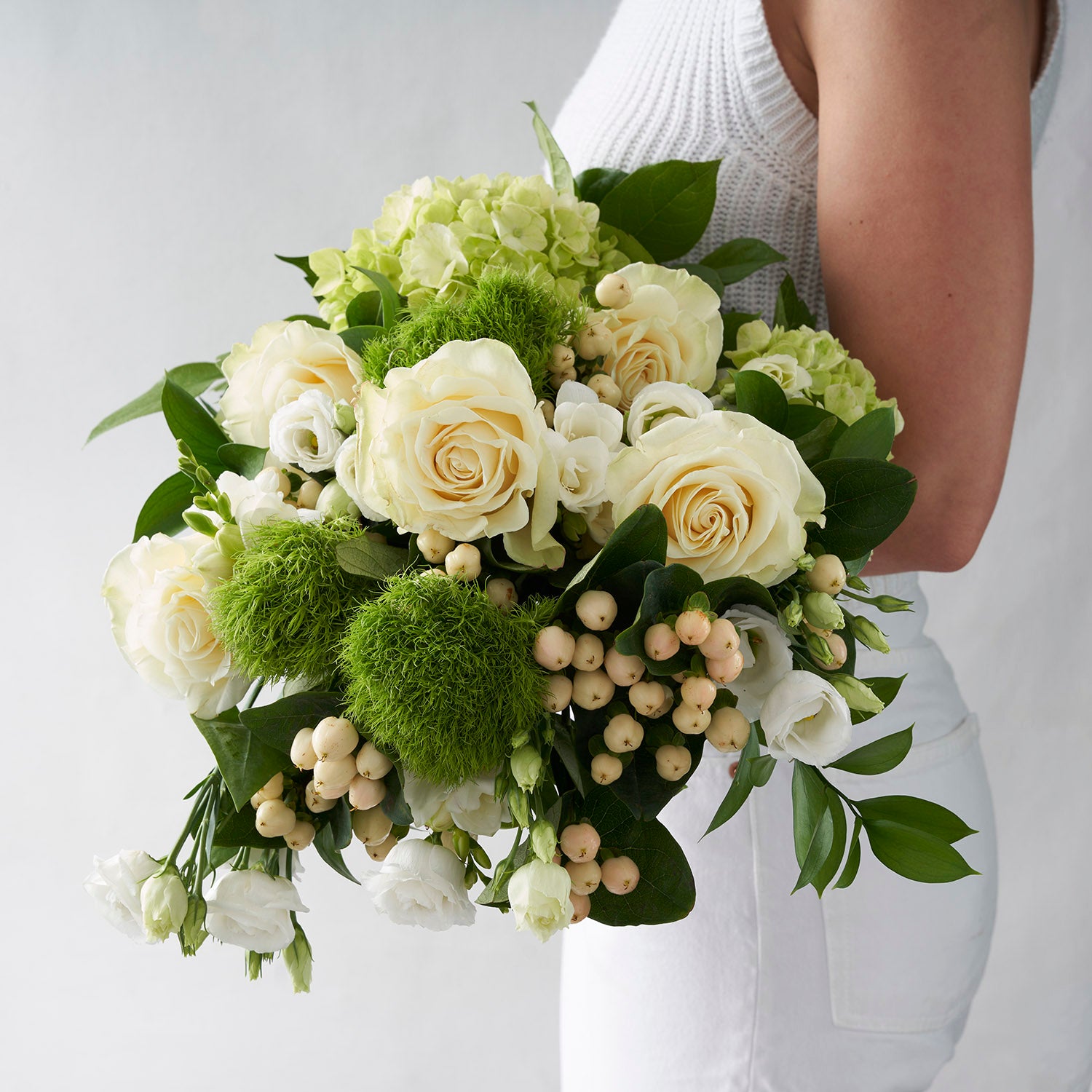 Woman in white holding white roses, cream hypericum berries, and green dianthus.