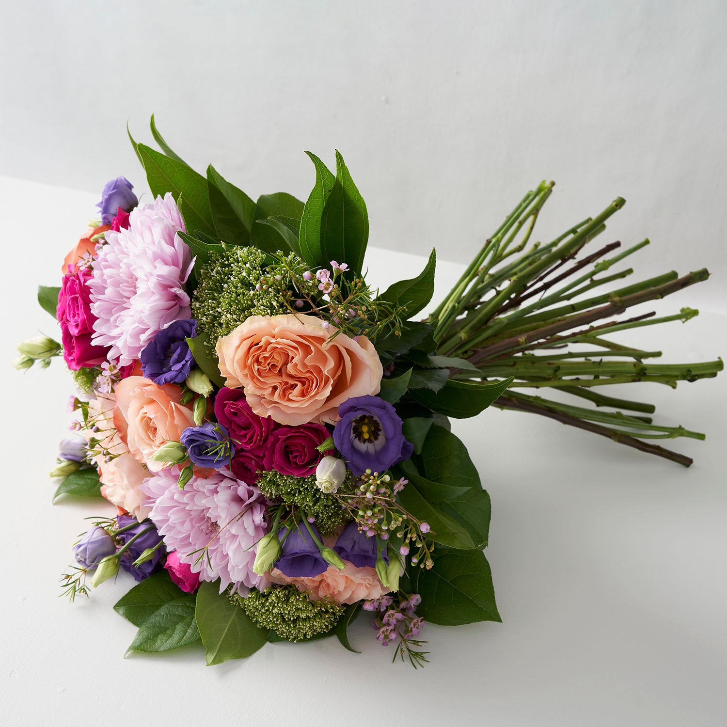 Side view of a handtied bouquet of lavender chrysanthemums, peach roses, fuchsia spray roses and purple lisianthus on white background.