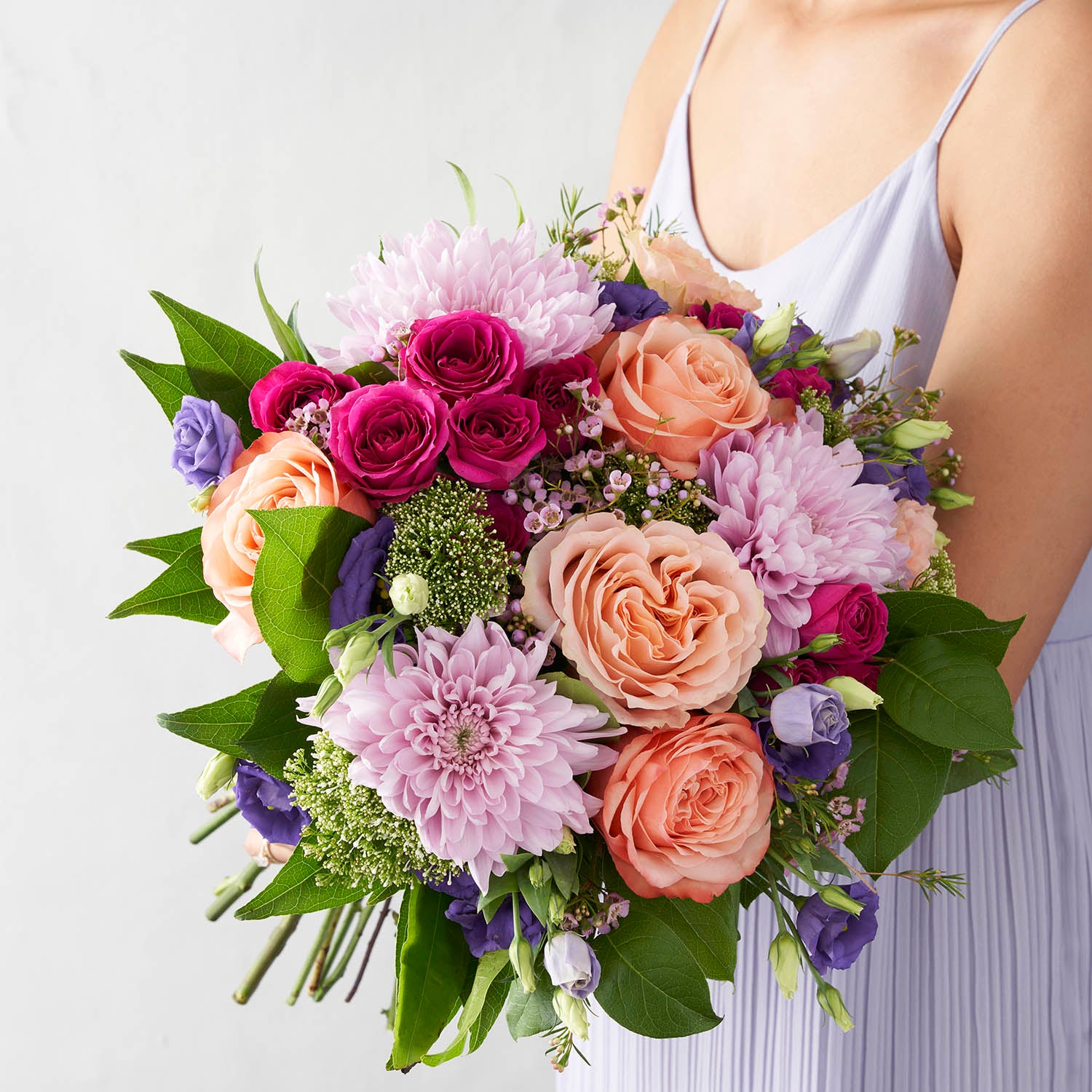 Woman in lavender dress holding bouquet of lavender chrysanthemums, peach roses, fuchsia spray roses and purple lisianthus.