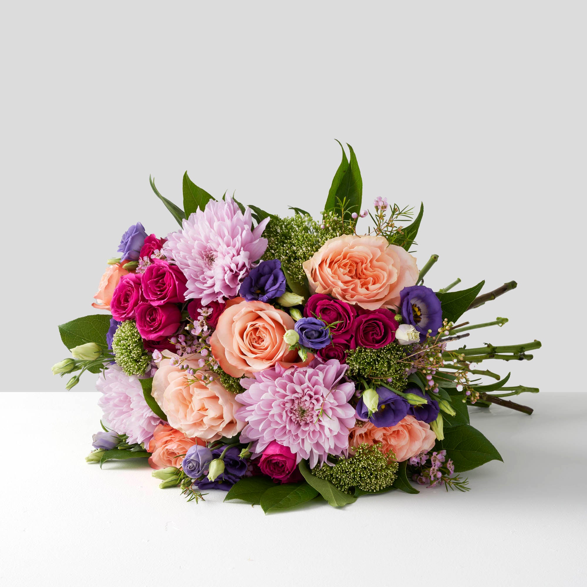 Handtied bouquet of lavender chrysanthemums, peach roses, fuchsia spray roses and purple lisianthus on white background.