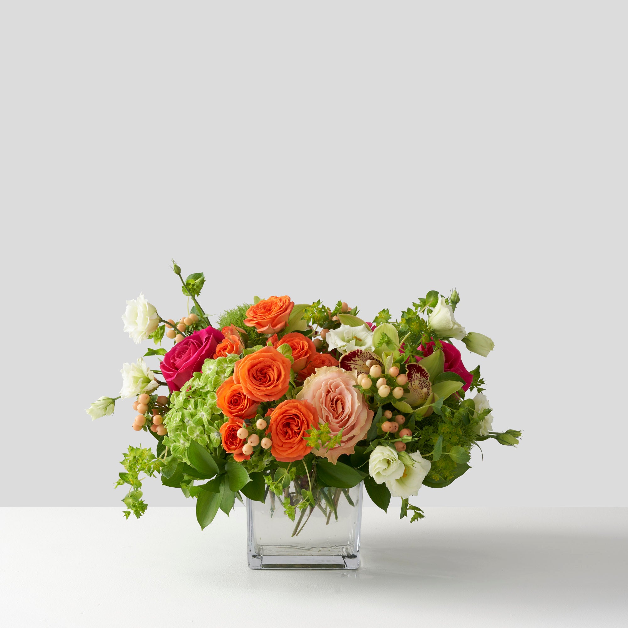 LIme green, orange, hot pink, pale pink flowers arranged in glass vase on white backgound.