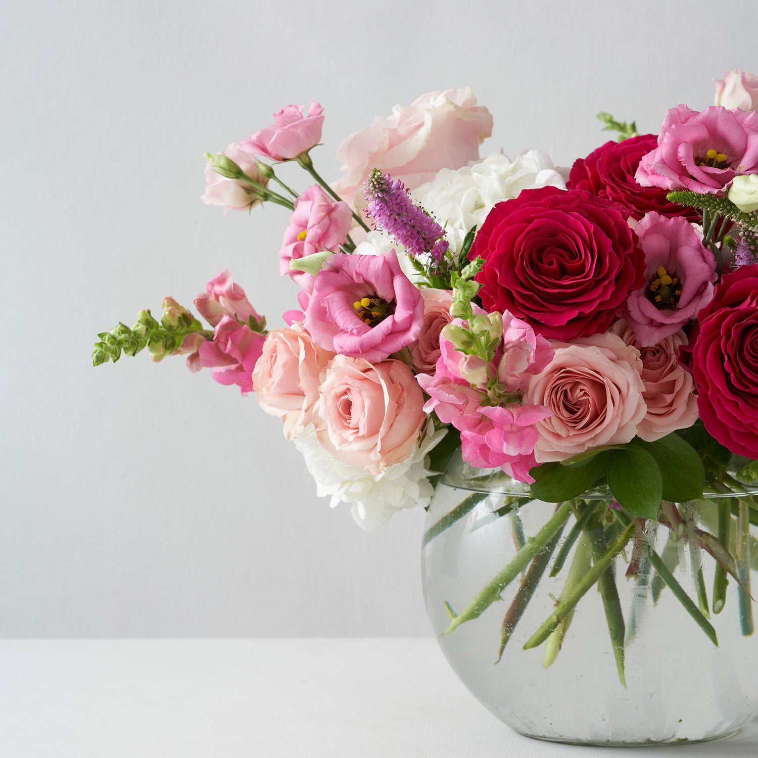 Various shades of pink flowers arranged in clear glass bowl,on white background.
