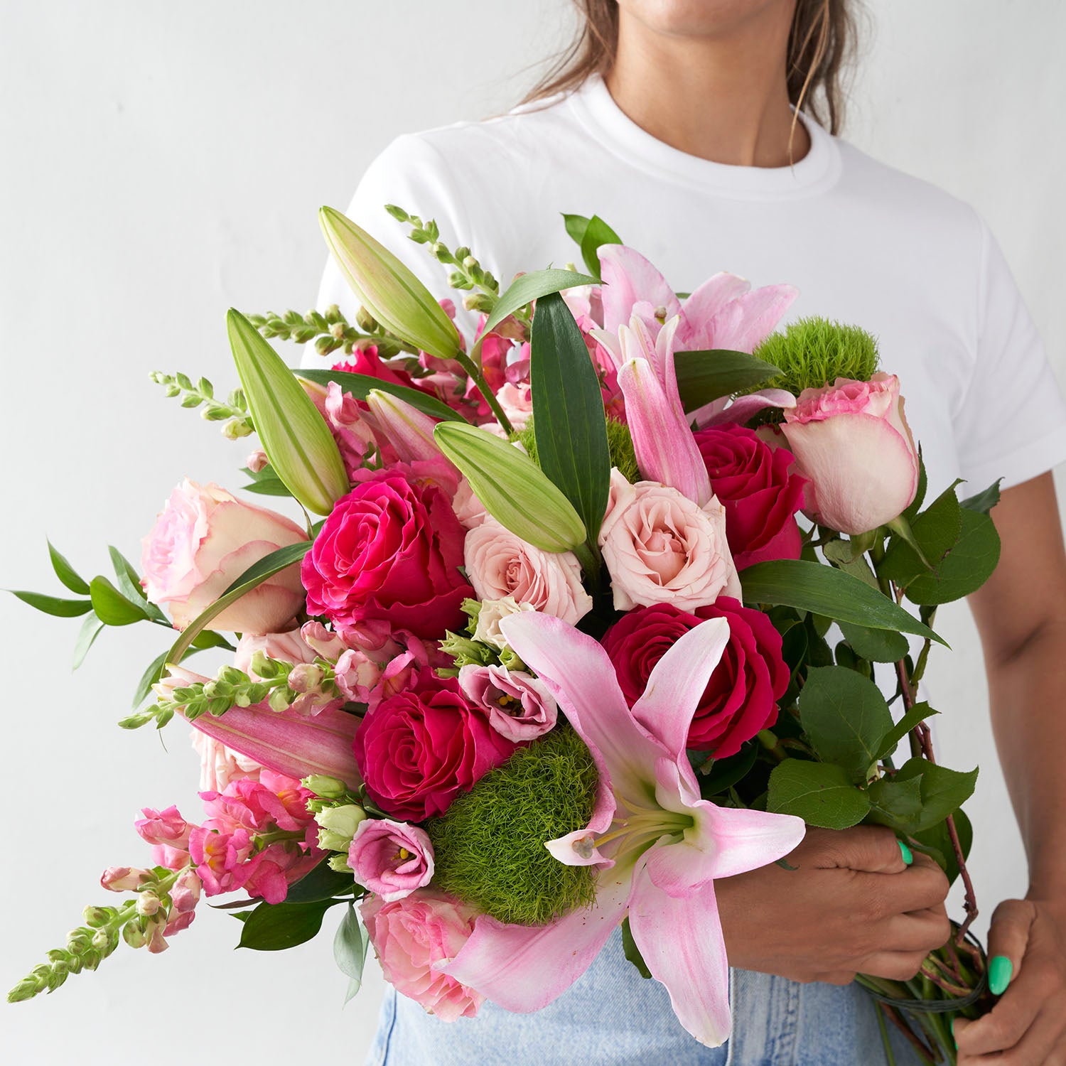 Woman in white t-shirt and jeans holding large bouquet of pink flowers.