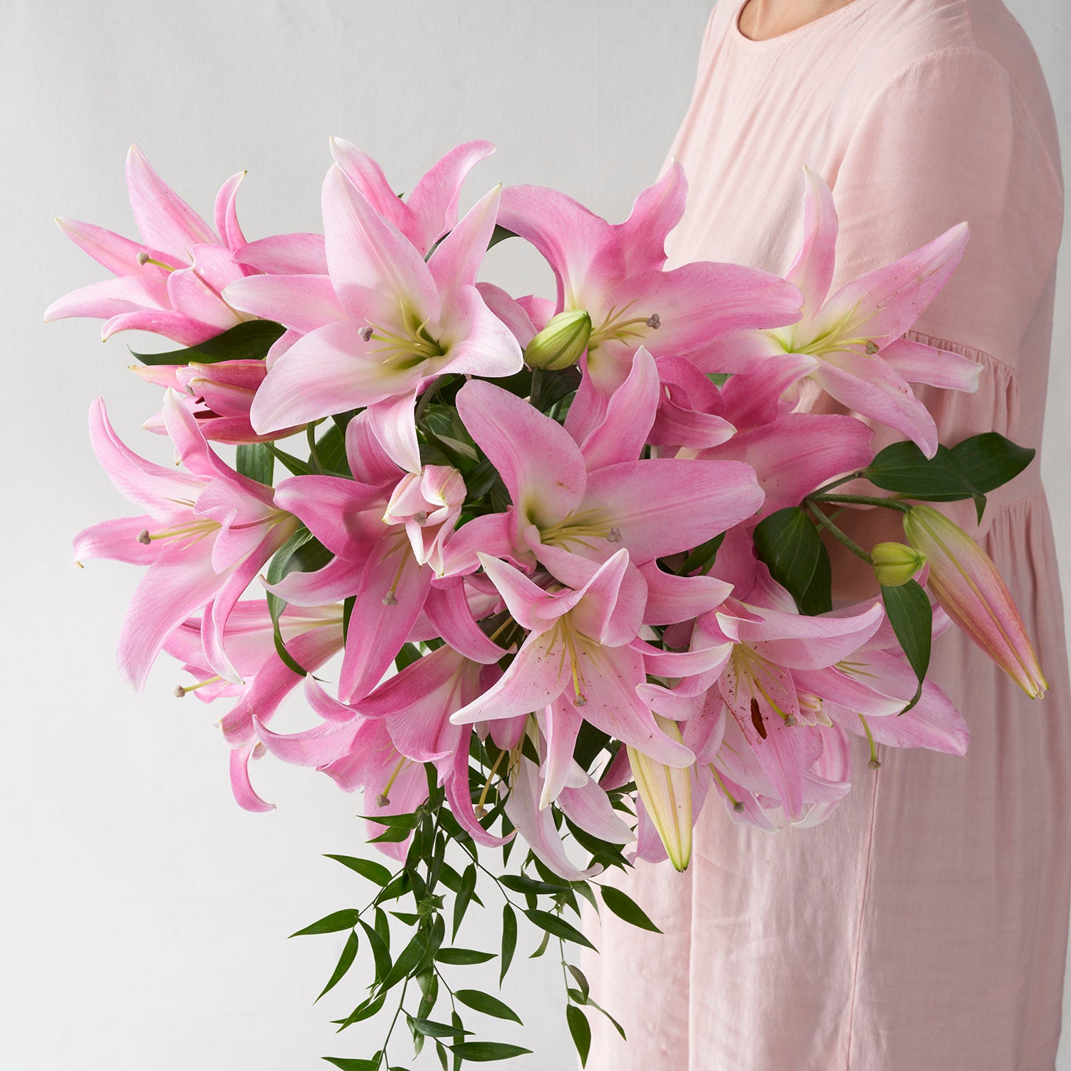 Woman in pale pink dress holding large bouquet of pink lilies.