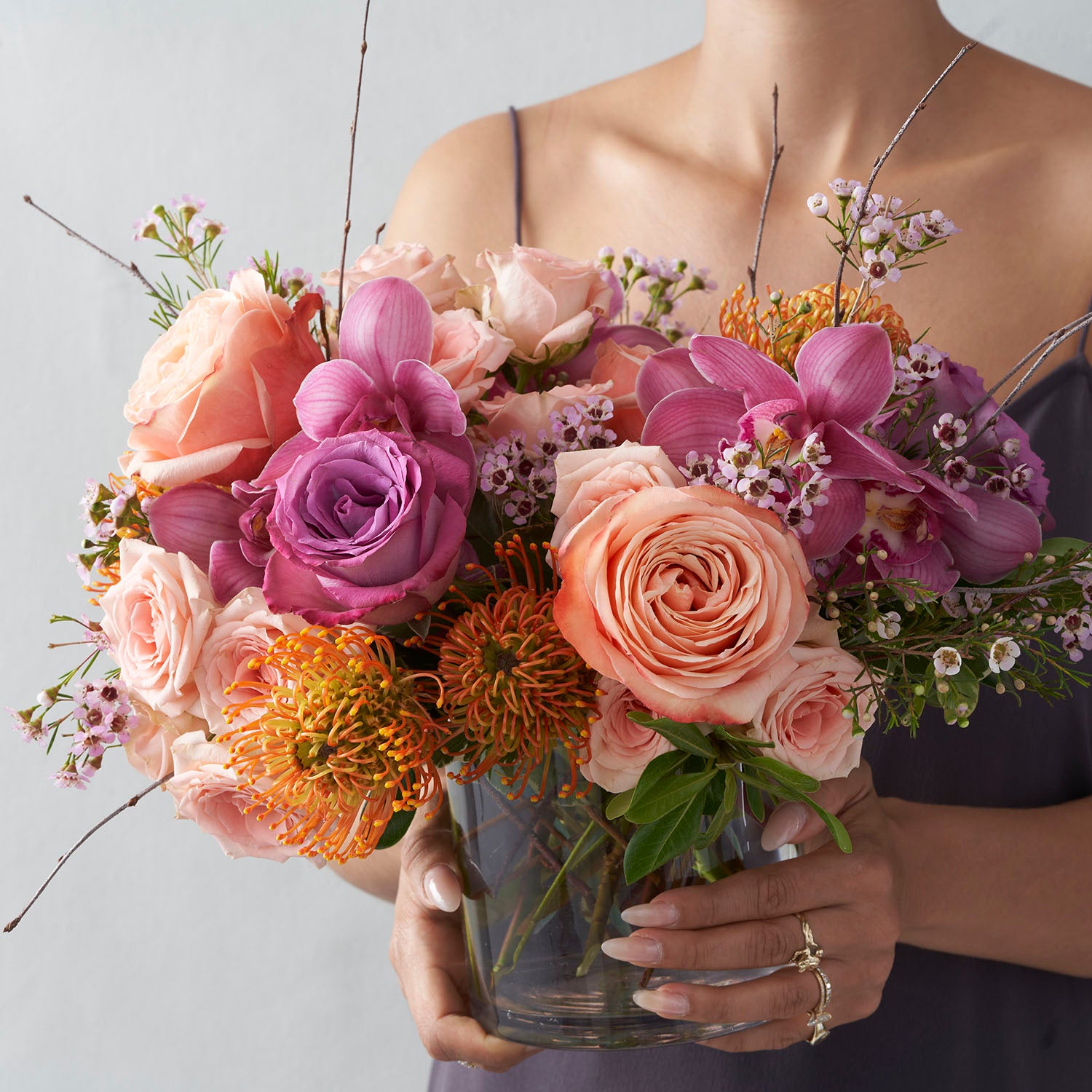 Woman in lavender dress holding peach, plum, and gold arrangement.