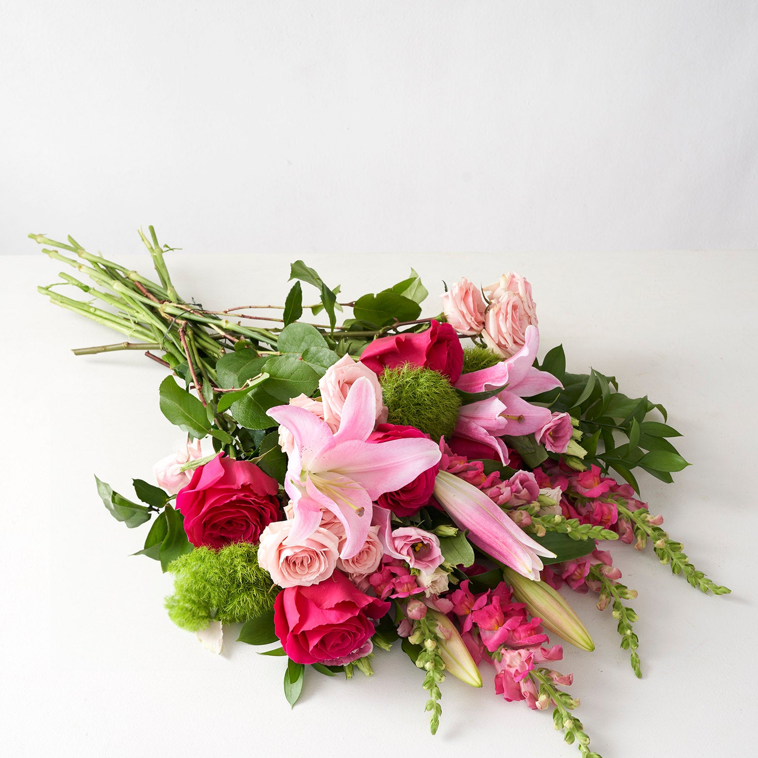 Bouquet of pink flowers including snapdragon, lilies, and roses on white background.