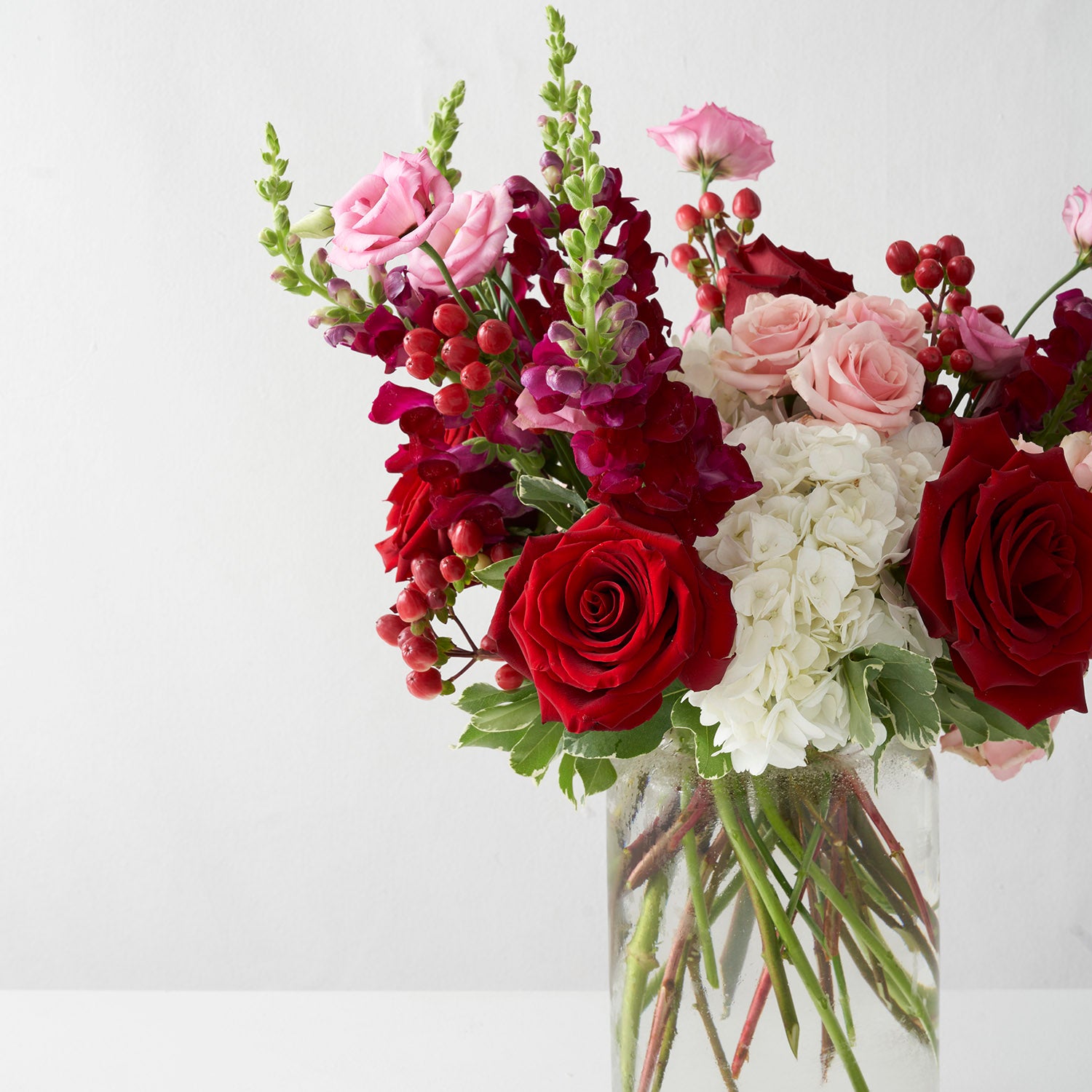 Red,pink and white arrangement, including hydrangea and roses, in glass vase on white background.