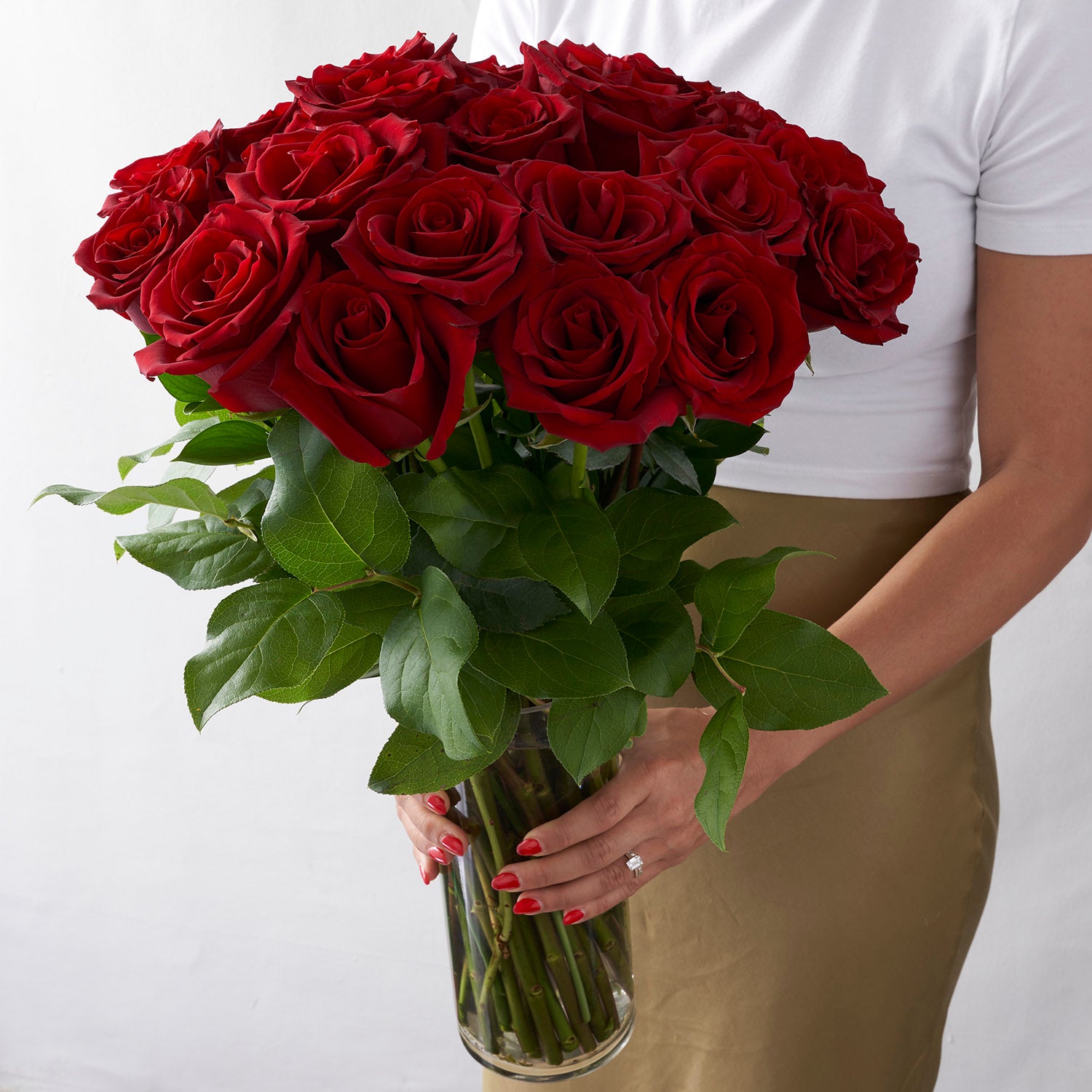 Woman holding glass vase full of 24 red explorer roses with greenery.
