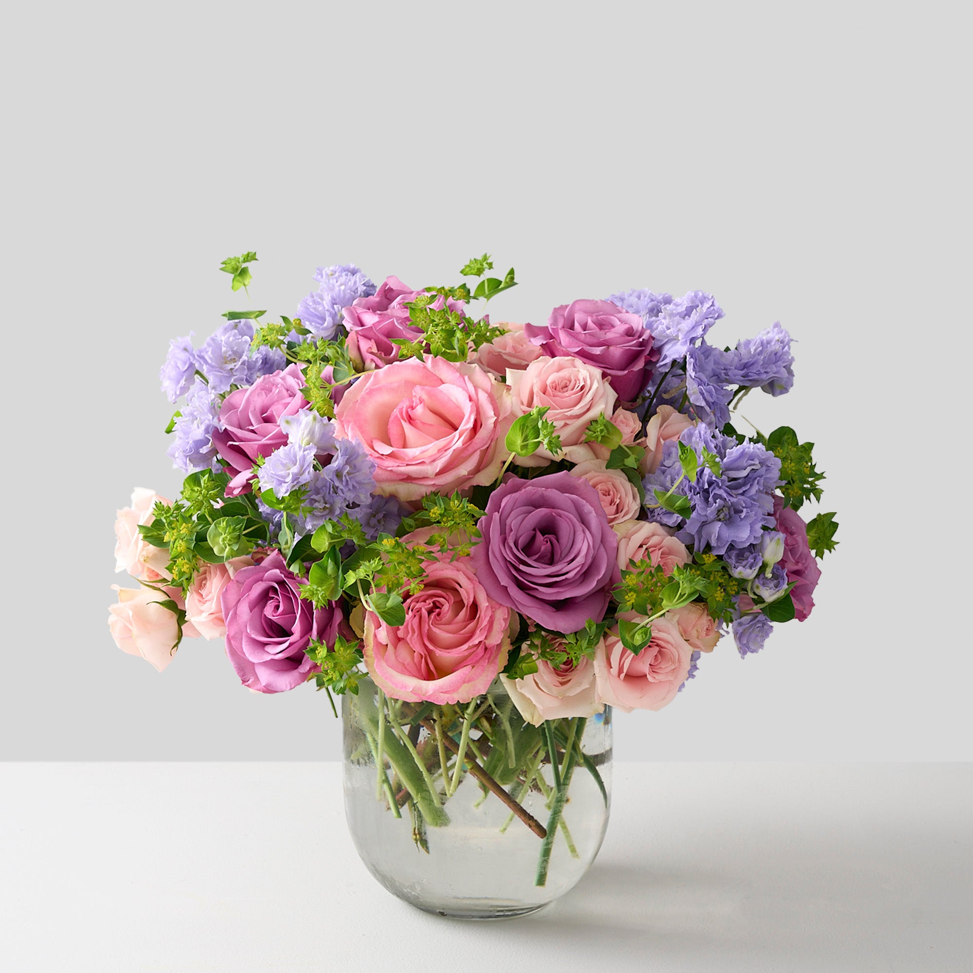 soft pink spray roses, green Bupleurum, lavender delphinium, Piacere roses, and Esperance Arranged in a round-bottom vase