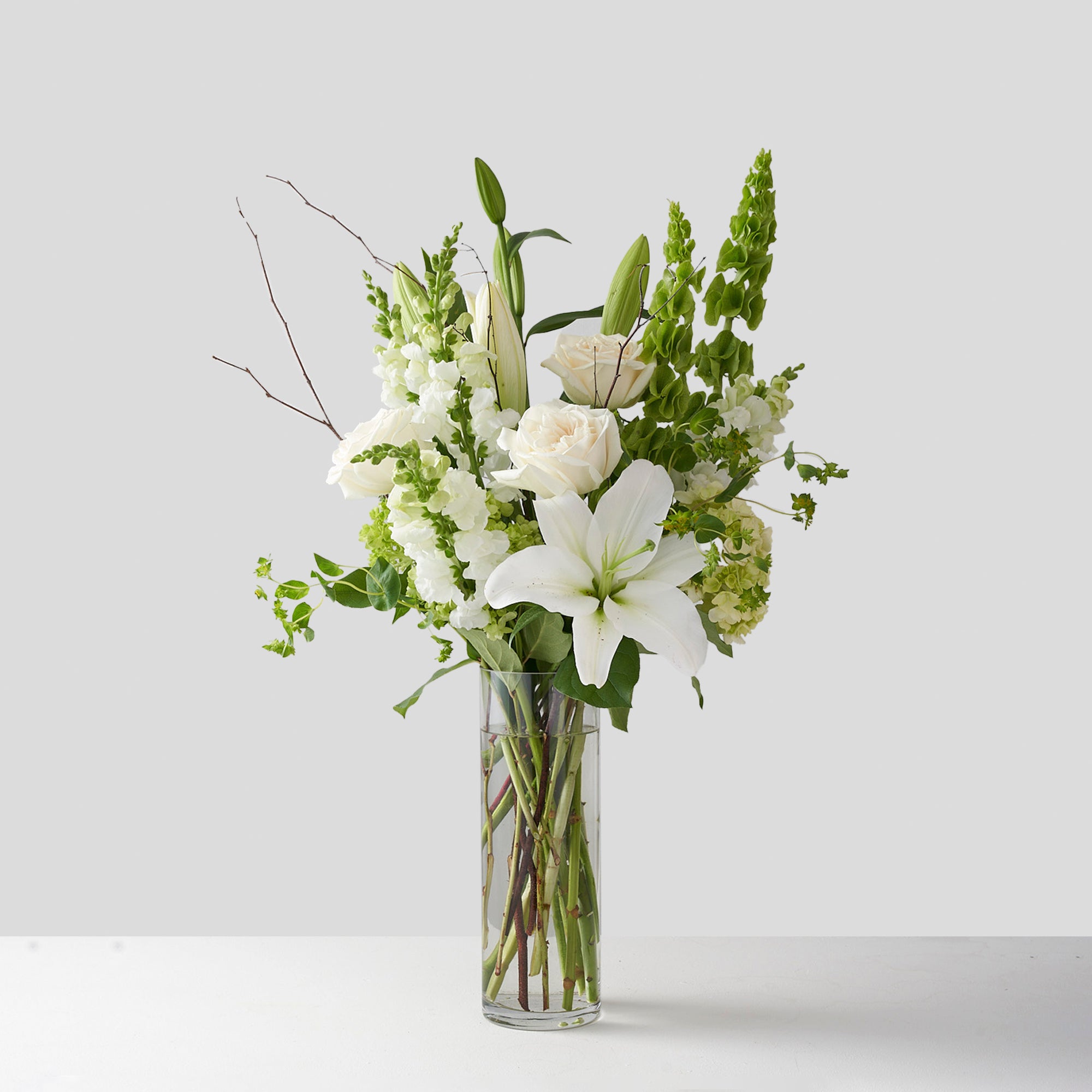 Small clear glass vase filled with white lilies, white roses, green hydrangea, and others