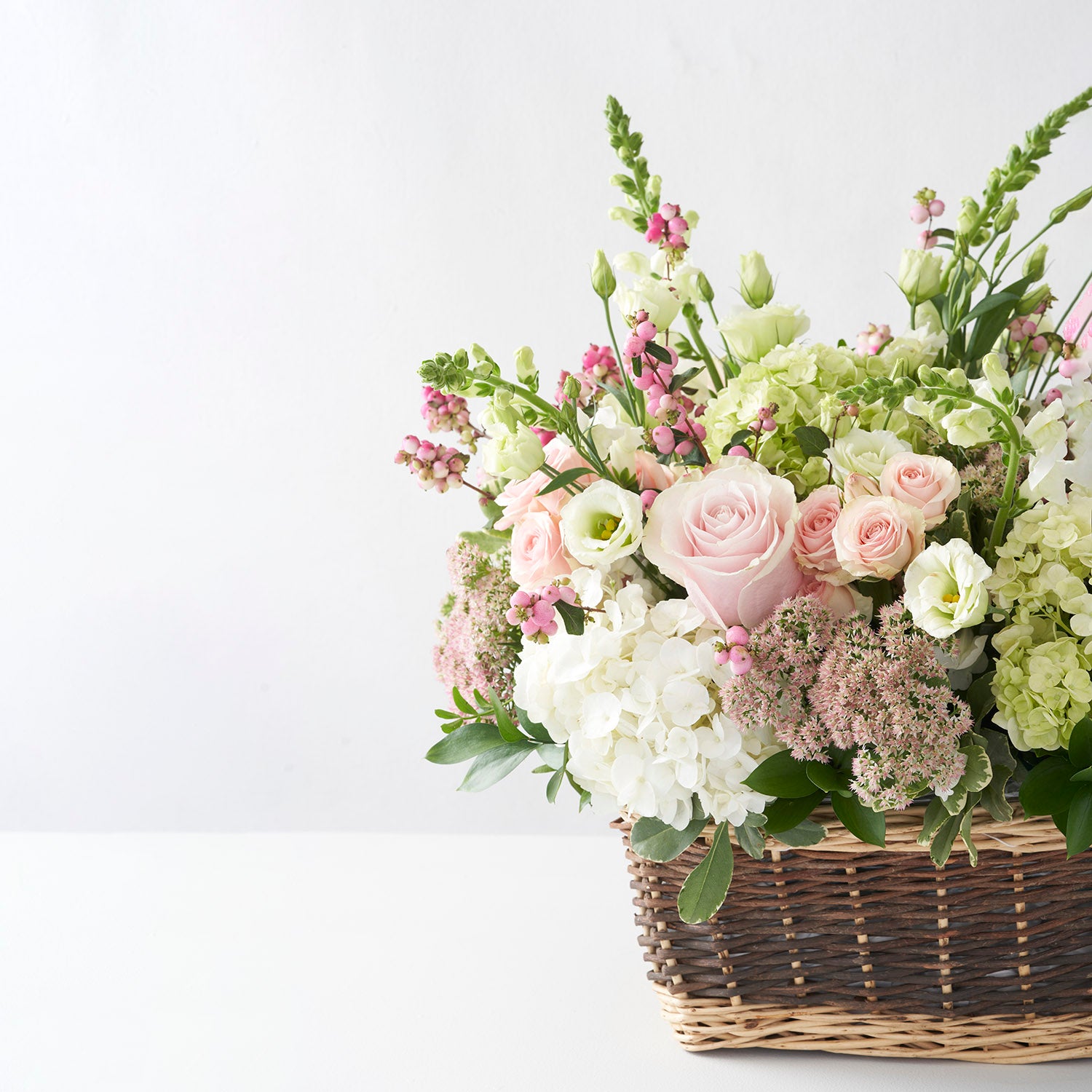 Natural basket filled with pale pink, white, and soft green flowers.