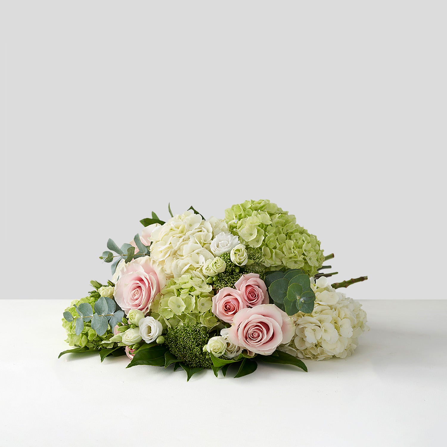 Bouquet of pink Mondial roses, green hydrangea, white lisianthus and eucalyptus on white background.