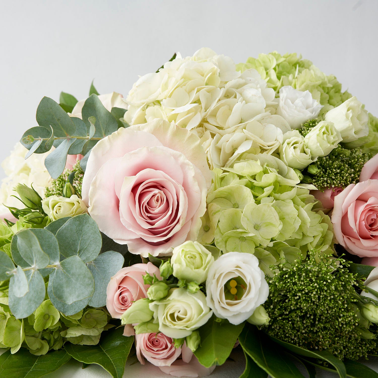 Closeup of pink Mondial roses, green hydrangea, white lisianthus and eucalyptus.