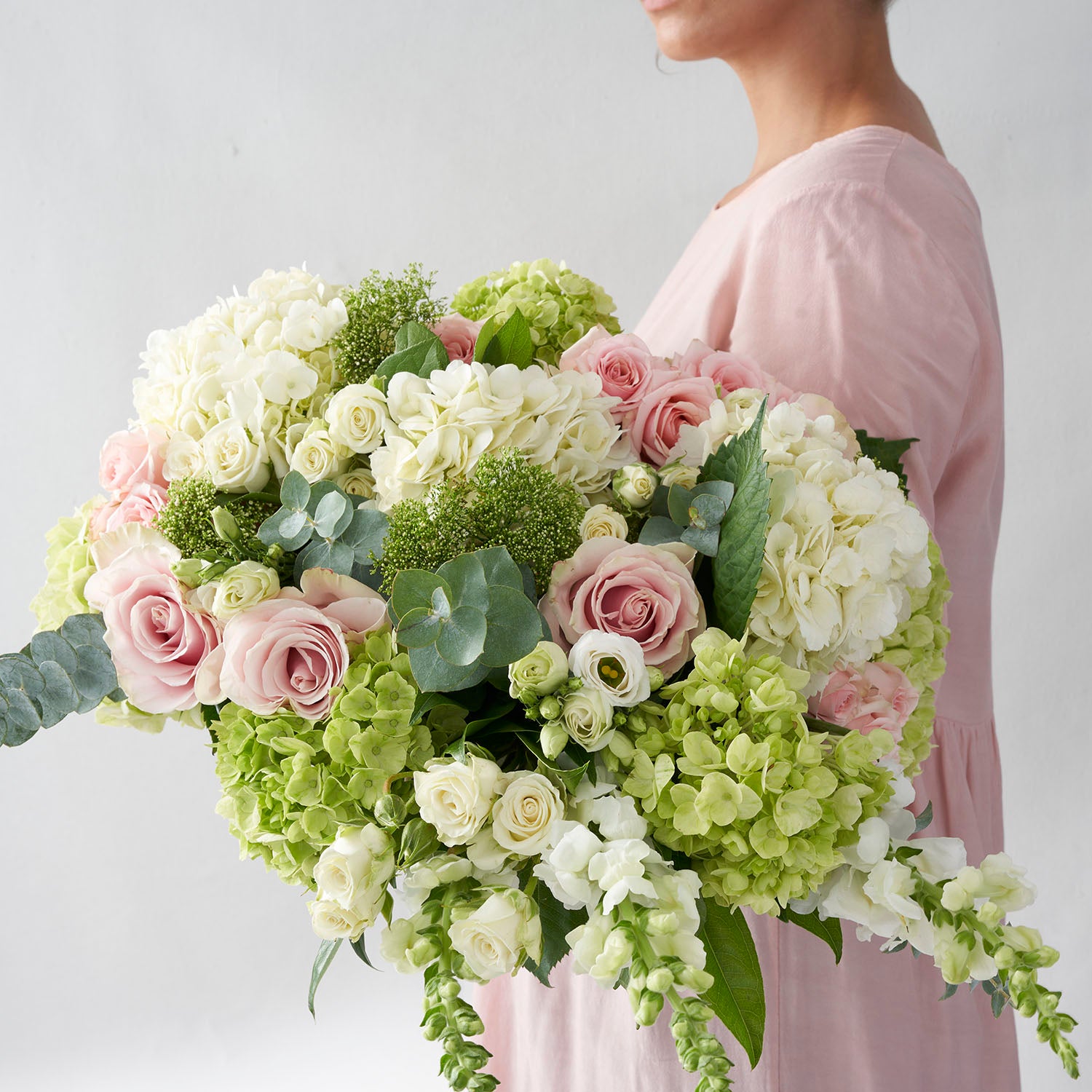 Woman in pink dress holding large bouquet of white, pale green, and pink flowers.