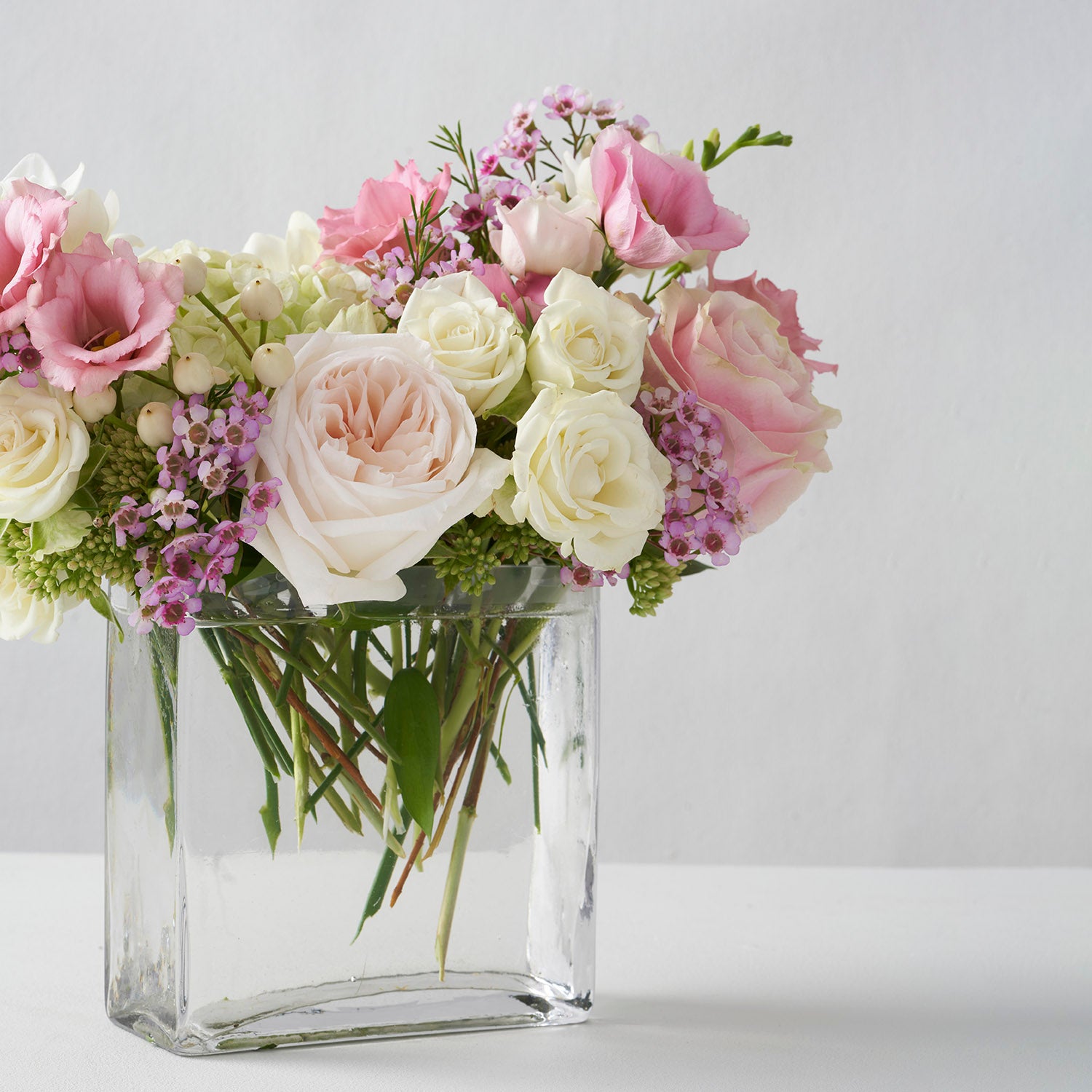 Rectangular glass vase filled with a mixture of soft pink flowers.