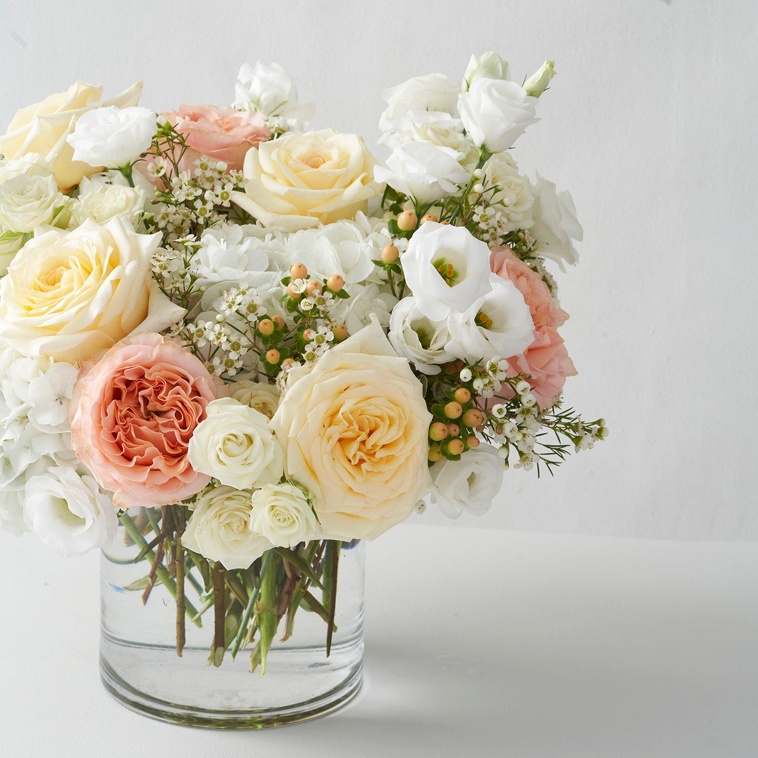 glass vase full of peach, cream and white flowers and berries.