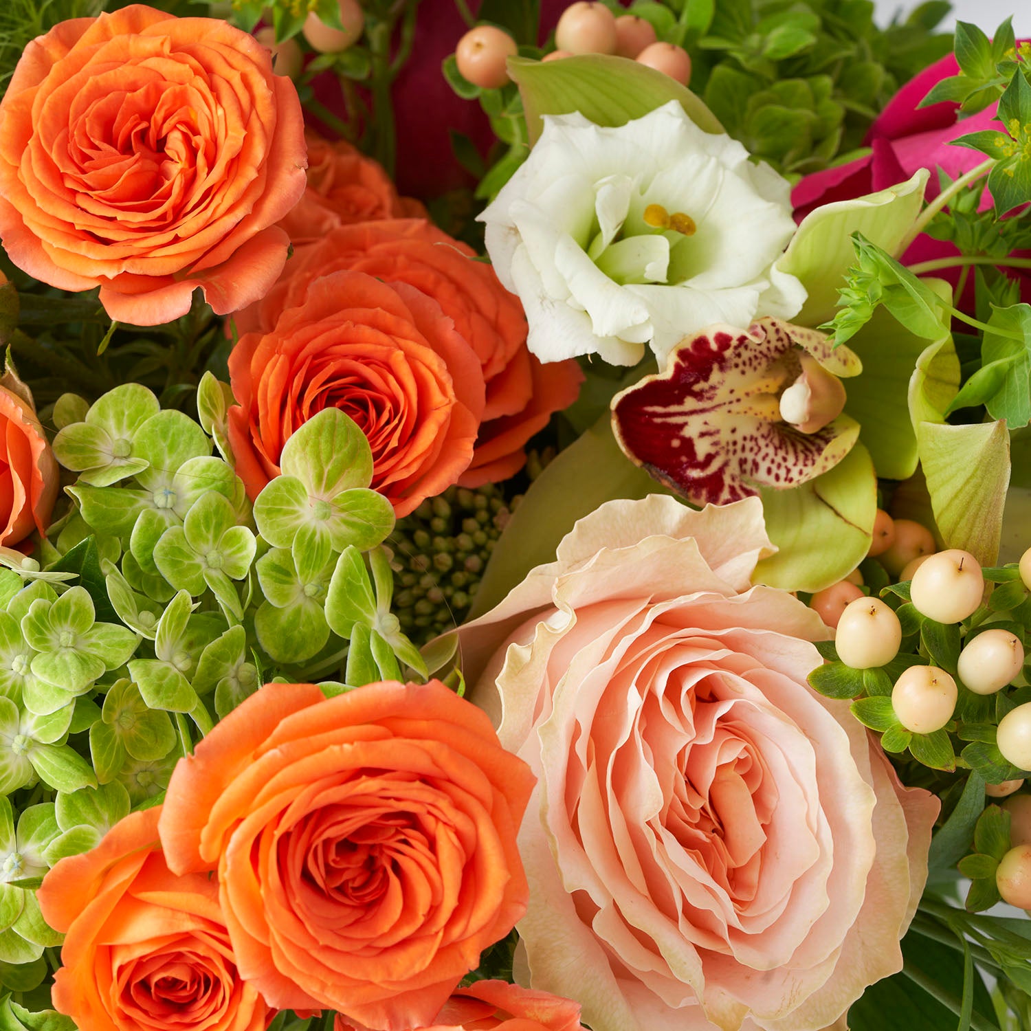 Closeup of orange spray roses, soft peach Princess Crown roses, green cymbidium flowers and green hydrangea.