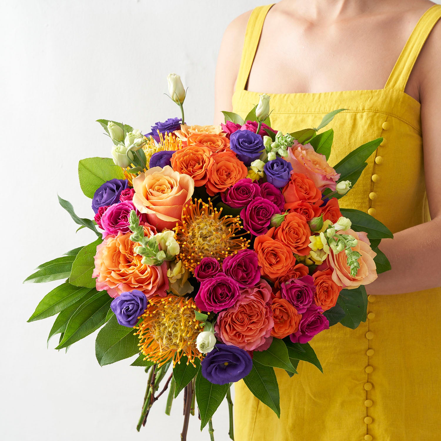 Woman in yellow dress holding bright orange, purple, and hot pink round bouquet.
