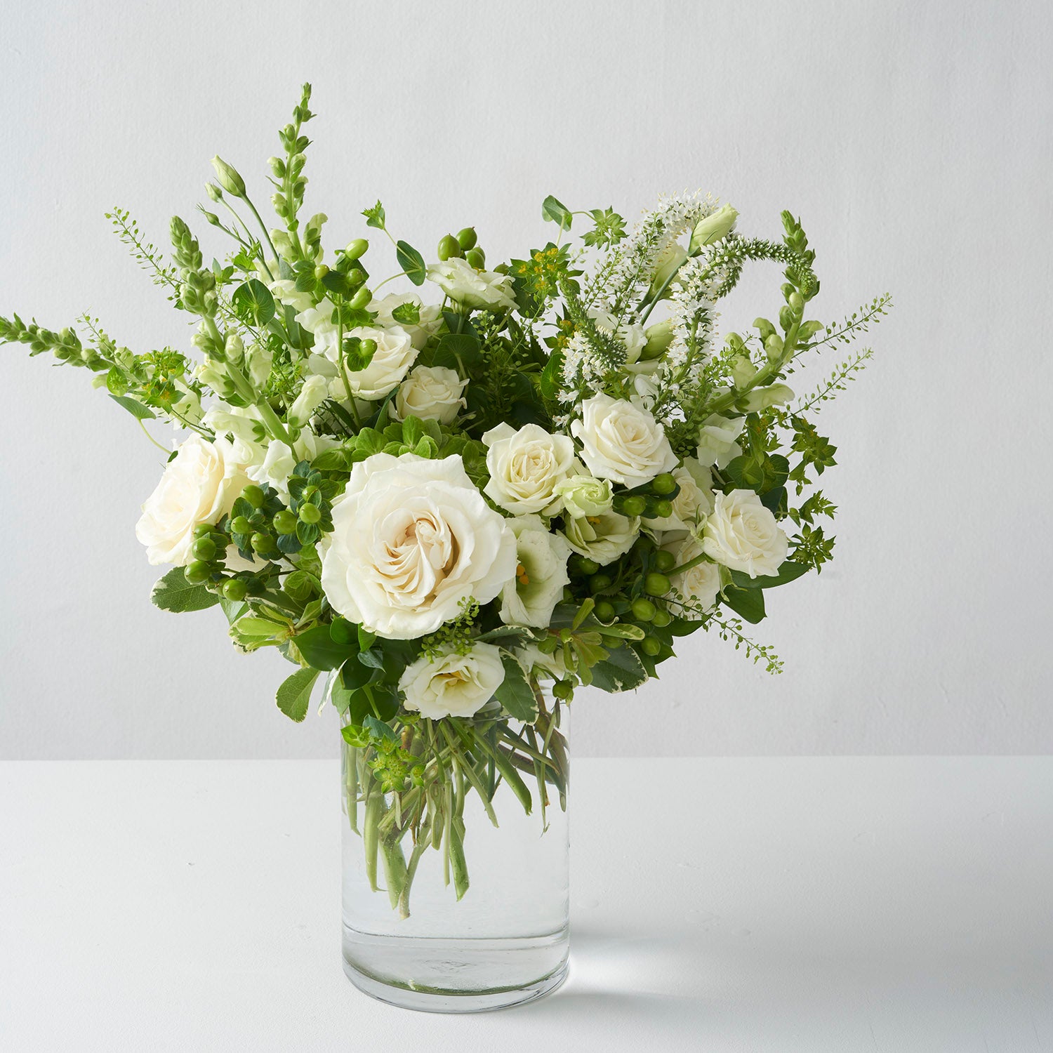 All white and green flowers in glass vase on white background.