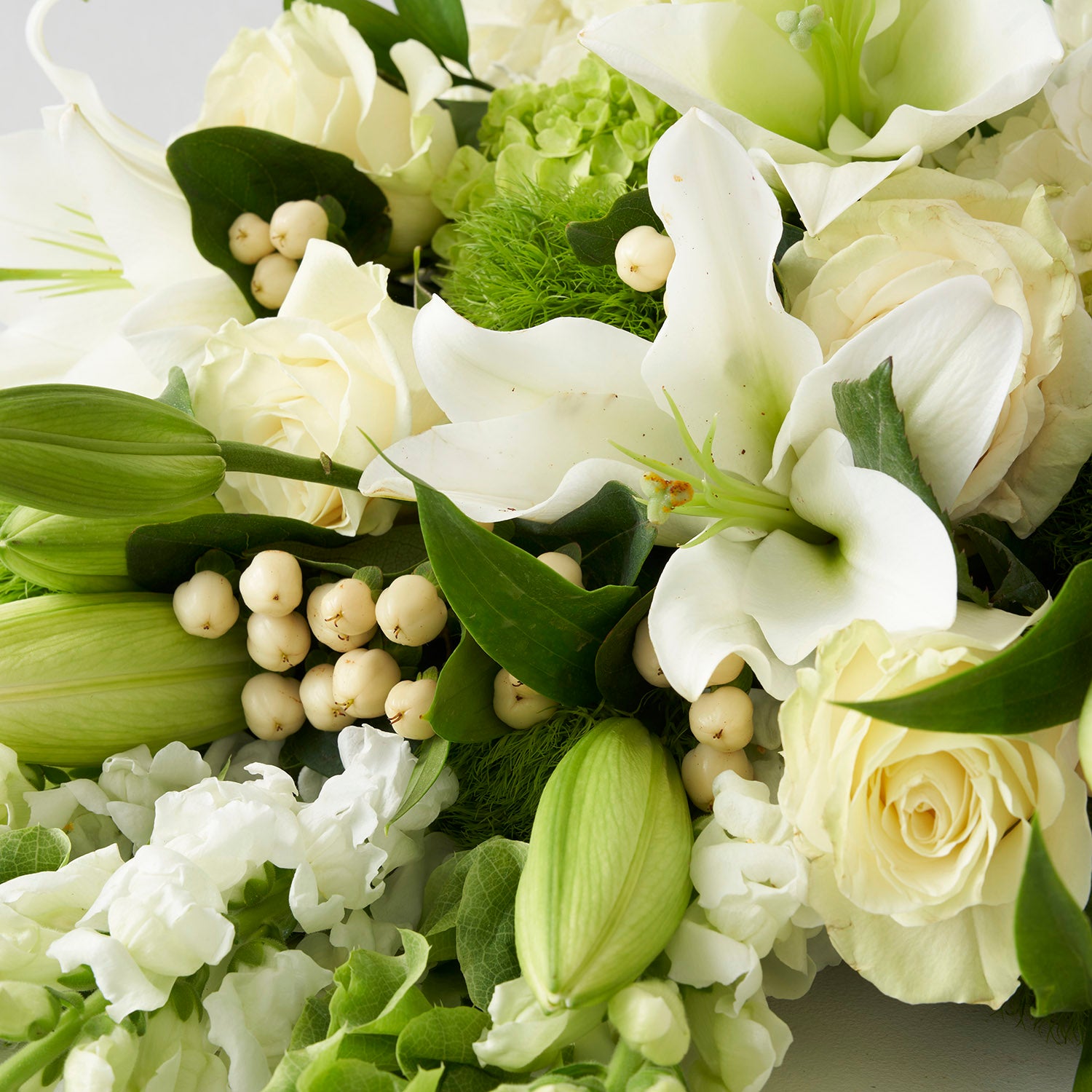 Closeup of white roses, white lilies, and cream berries.