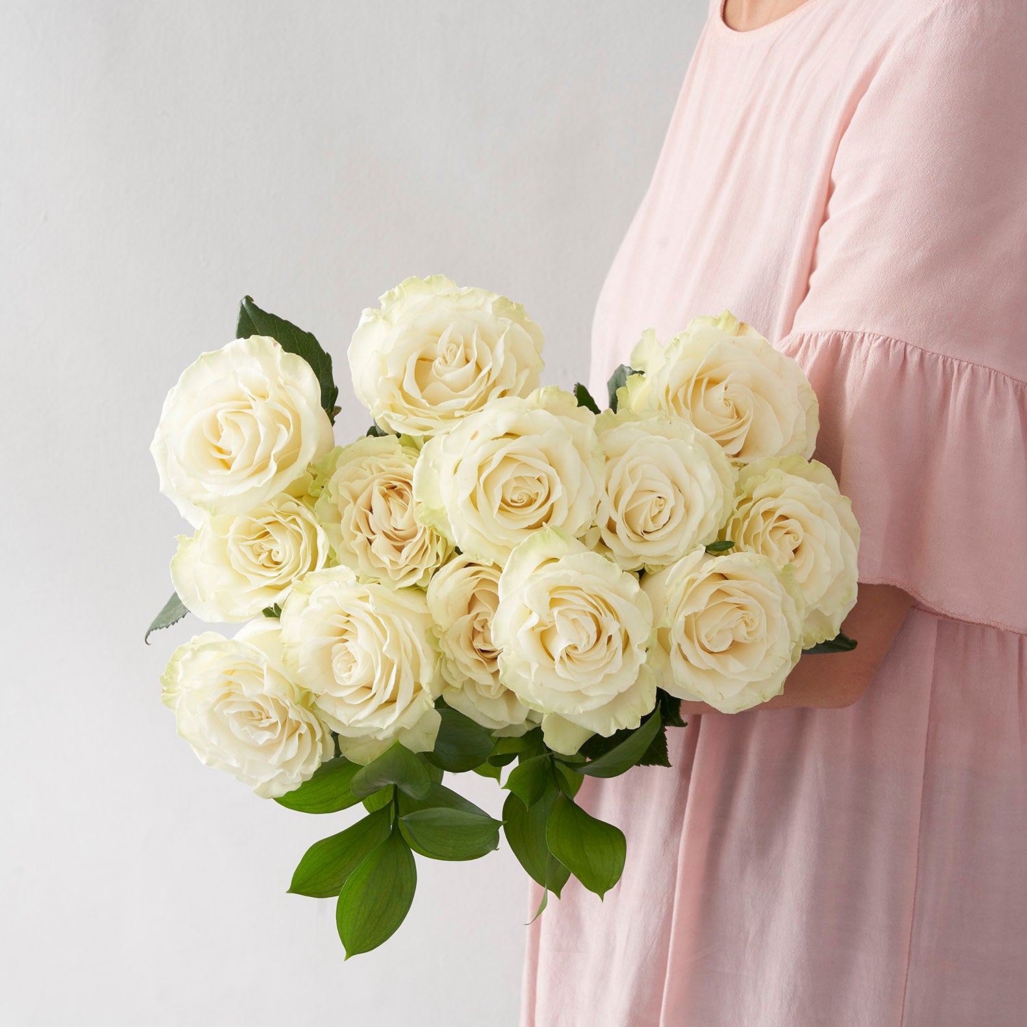Woman in pale pink dress holding bouquet of white Mondial roses.