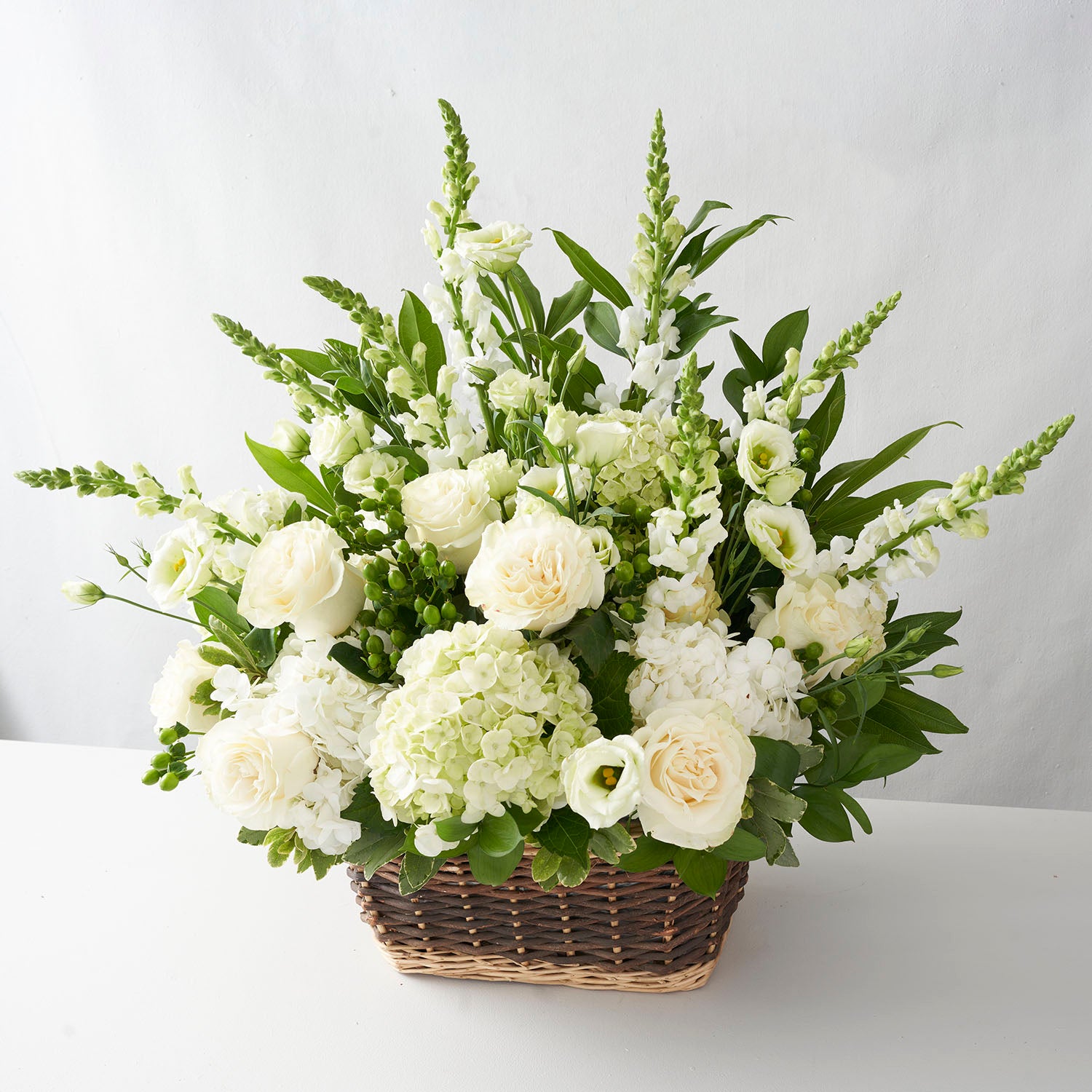 Large arrangement of all white flowers in a natural basket on a white background.