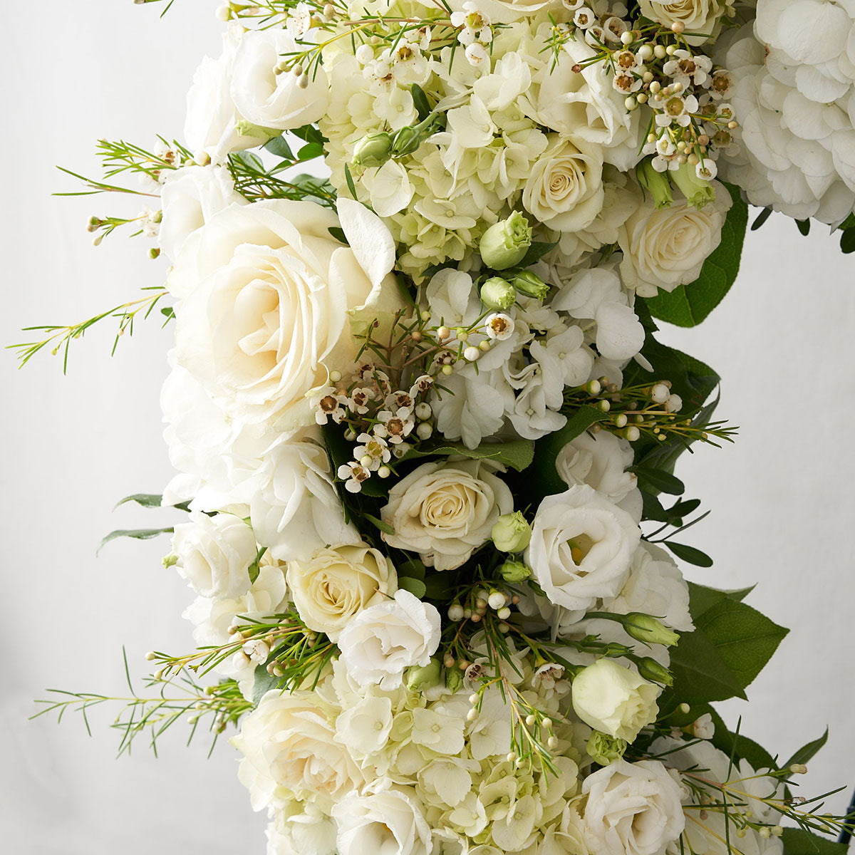 Close up of an assortment of white flowers and greenery, including roses, hydrangea, anemones, lilies, and others