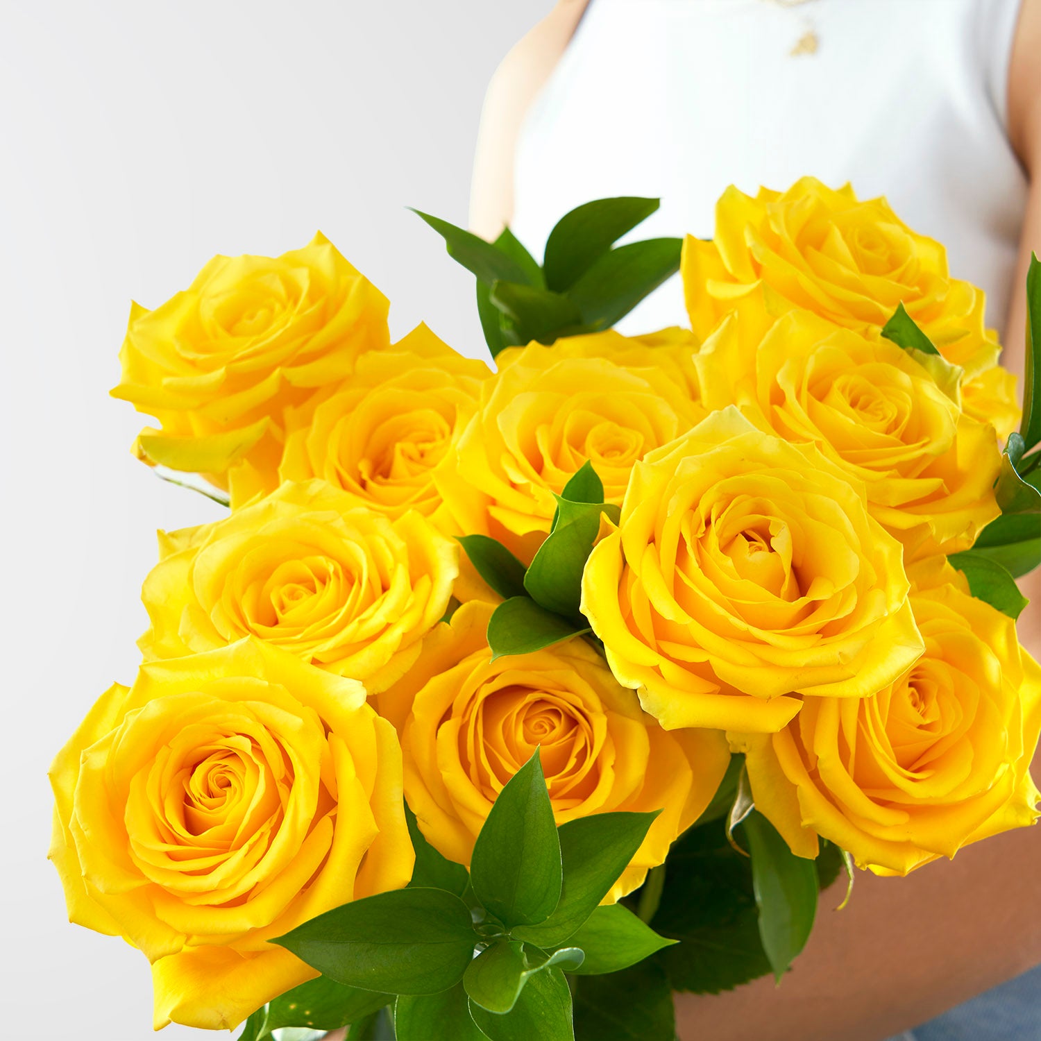 Close up of yellow roses, there is a blurry person holding them. 