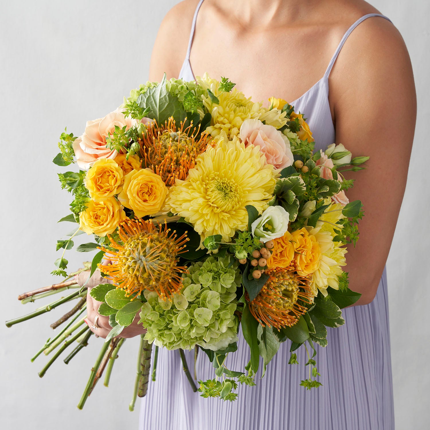woman in lavender dress holding yellow, gold ,and peach handtied bouquet.