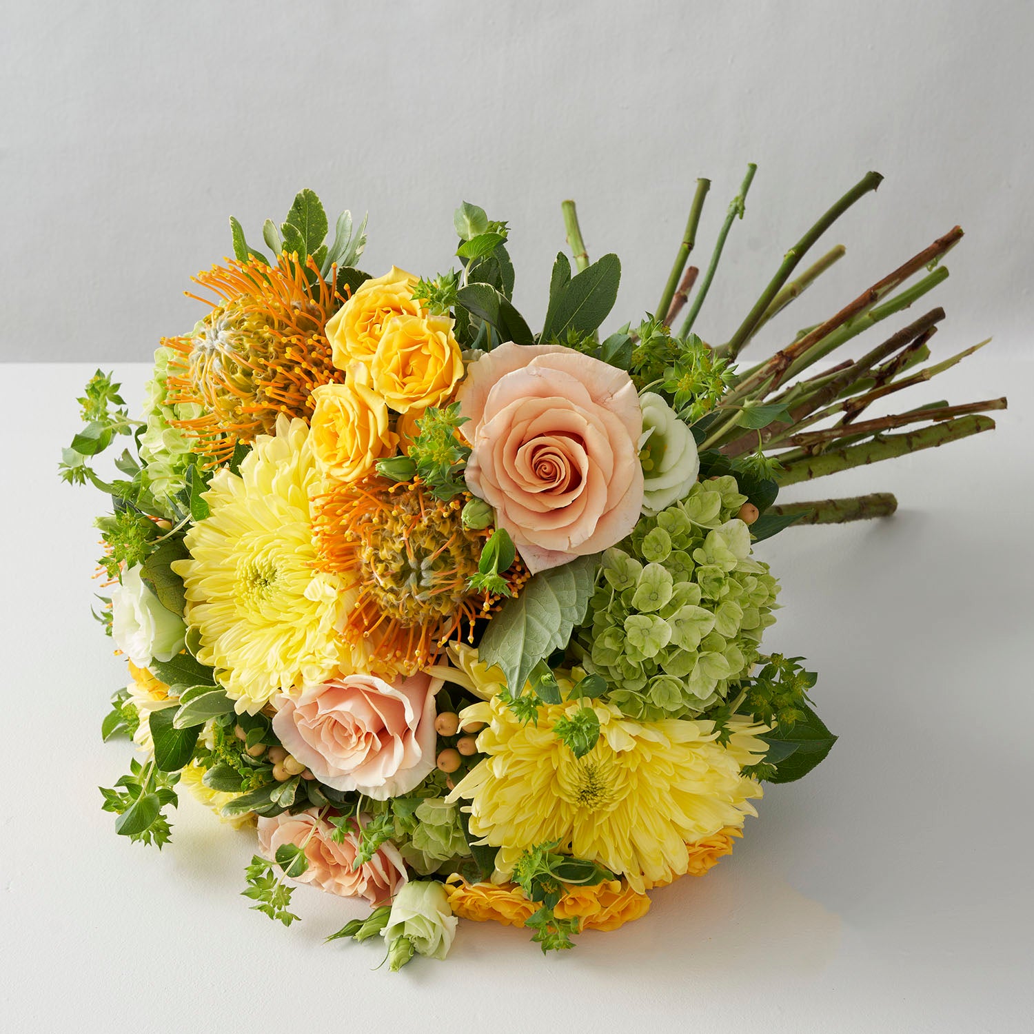Handtied bouquet of yellow chrysanthemums, peach roses, green hydrangea, peach hypericum berries and gold protea flowers on white background.