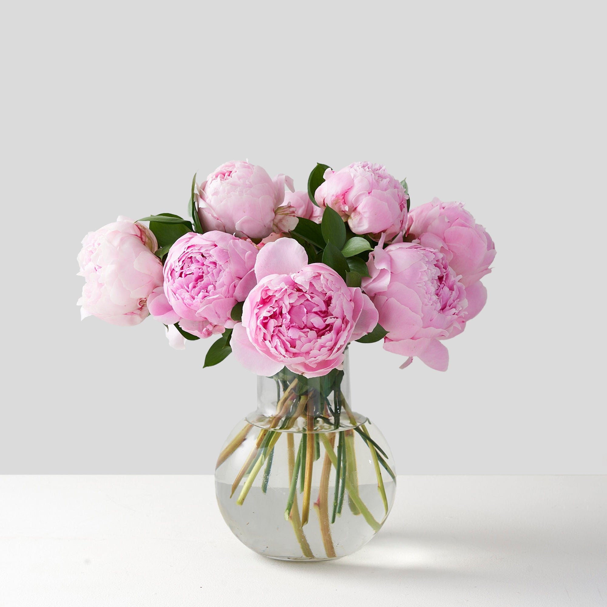 Round glass vase filled with pink peonies