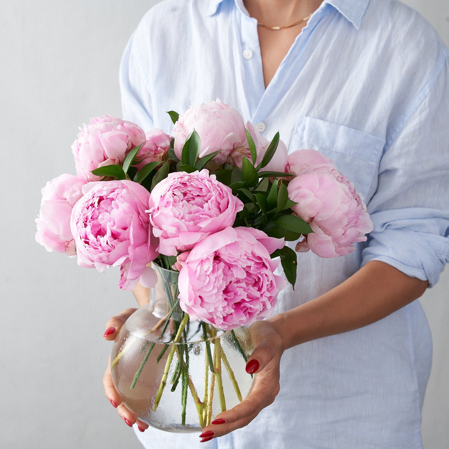 Woman in blue holding round glass vase filled with pink peonies