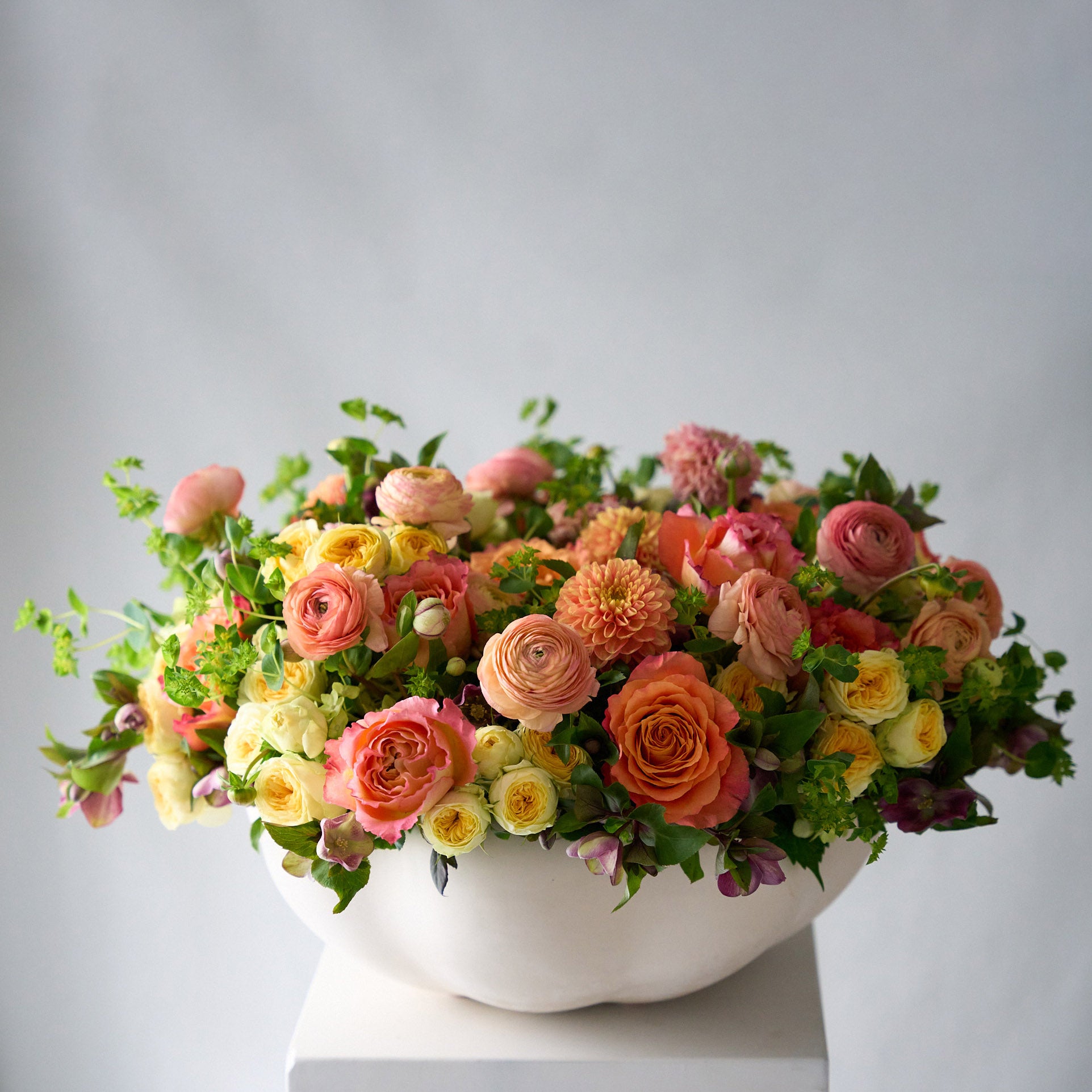 orange dahlias, peach ranunculus, double yellow Lisianthus, free spirit roses in a scalloped low oval white ceramic container 