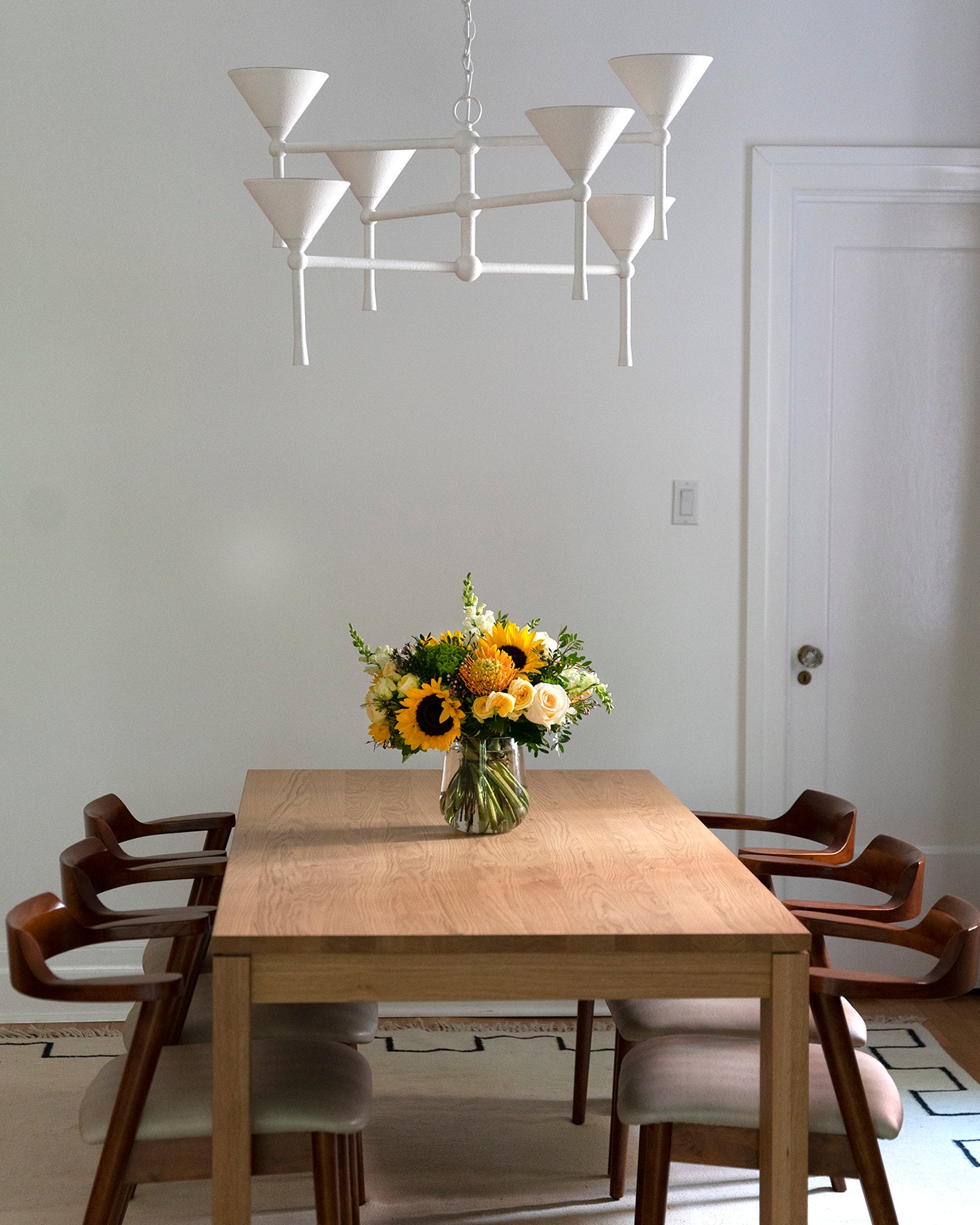 Clear glass vase arranged with orange spray roses, white roses, sunflowers,  and more plus greenery