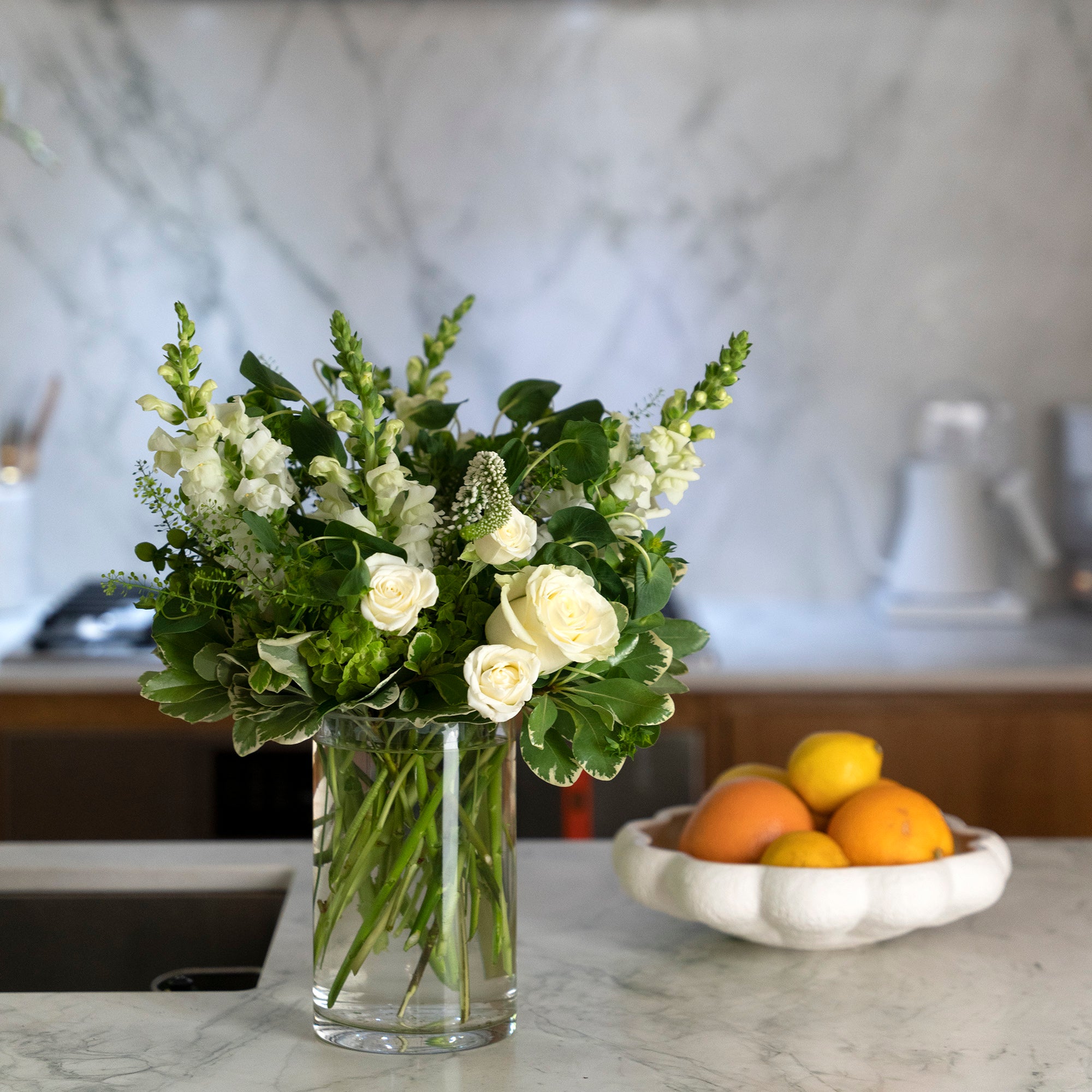 Cylindrical clear glass vase arranged with white roses, white spray roses, and greenery