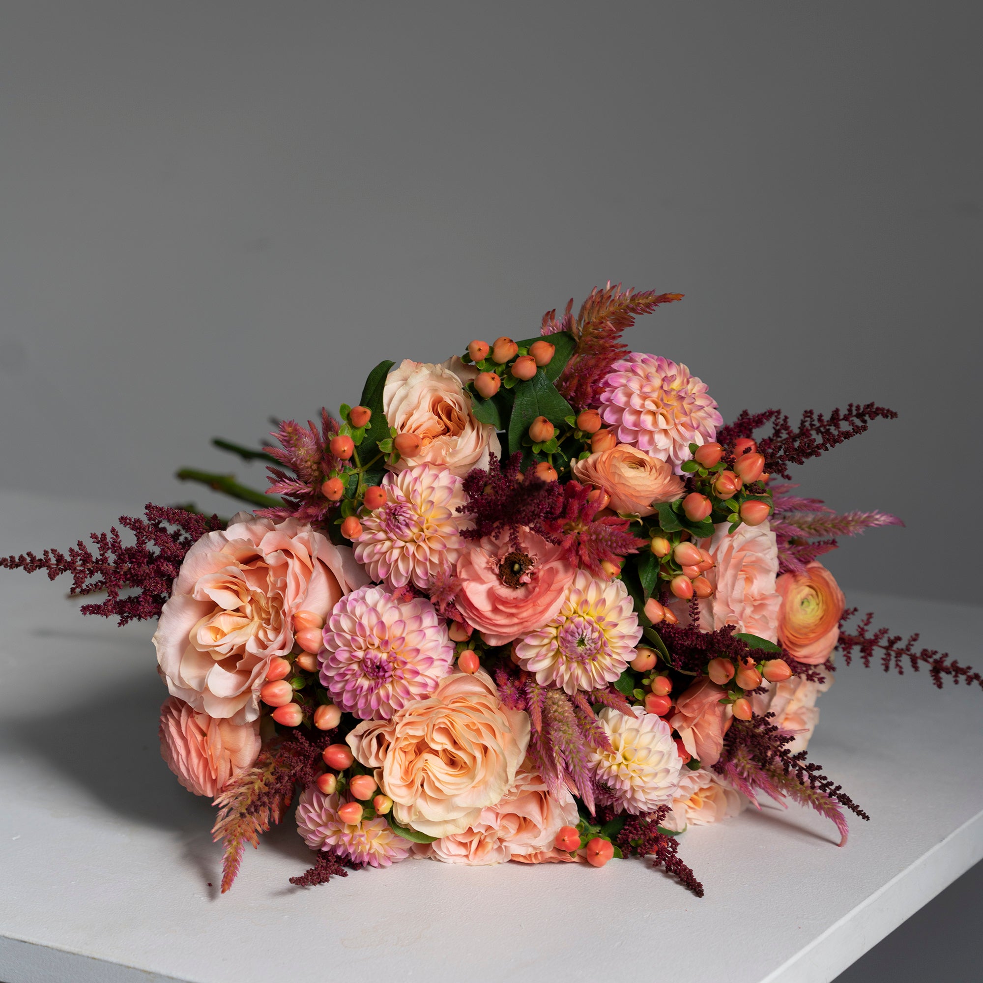 peach, coral colored hand tied bouquet with peach roses, pink dahlias and deep burgundy astilbe. 