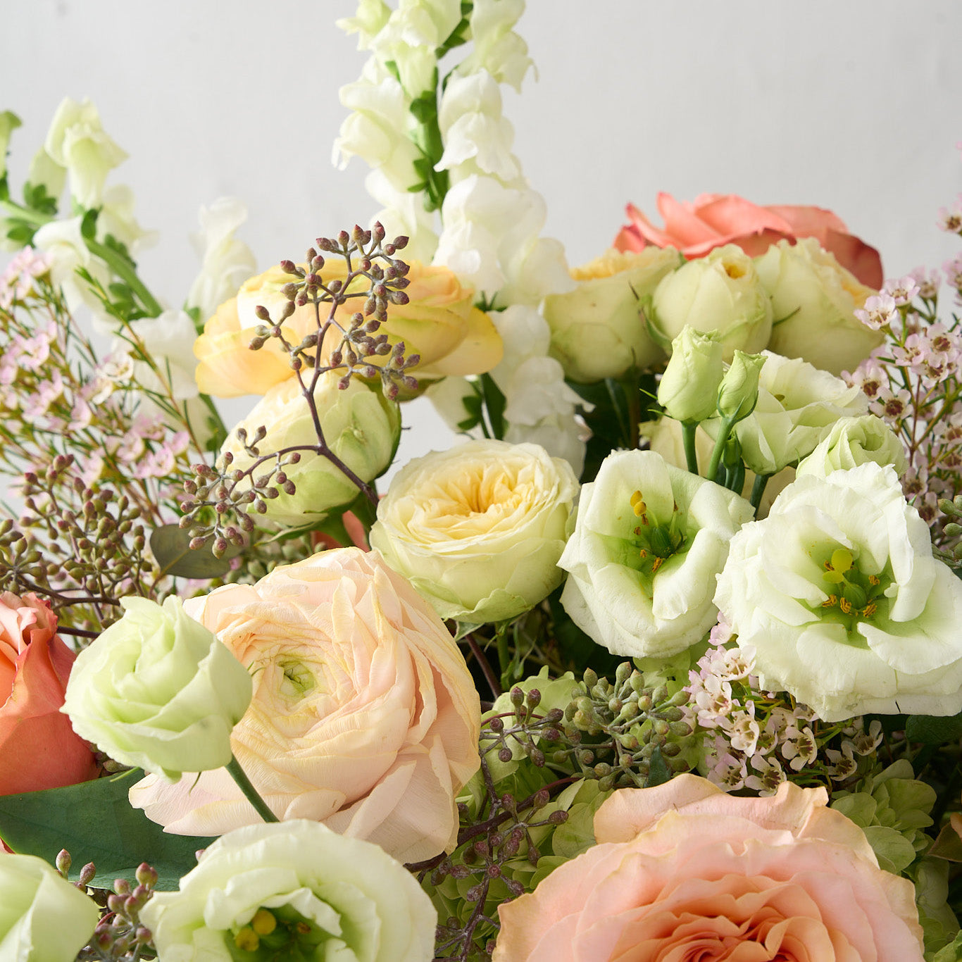 close up photo of white snapdragons and Lisianthus, cream double spray roses, peach roses, soft pink wax flowers and seeded eucalyptus