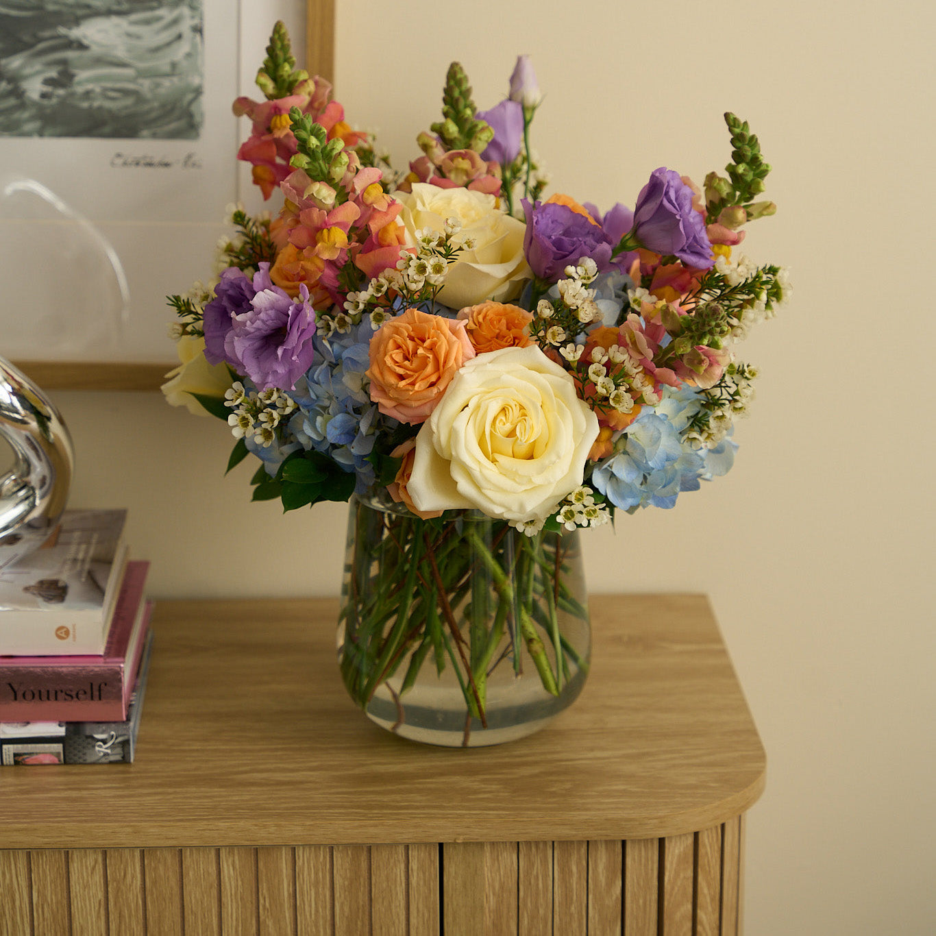 Spring flower bouquet in a clear vase on a brown credenza