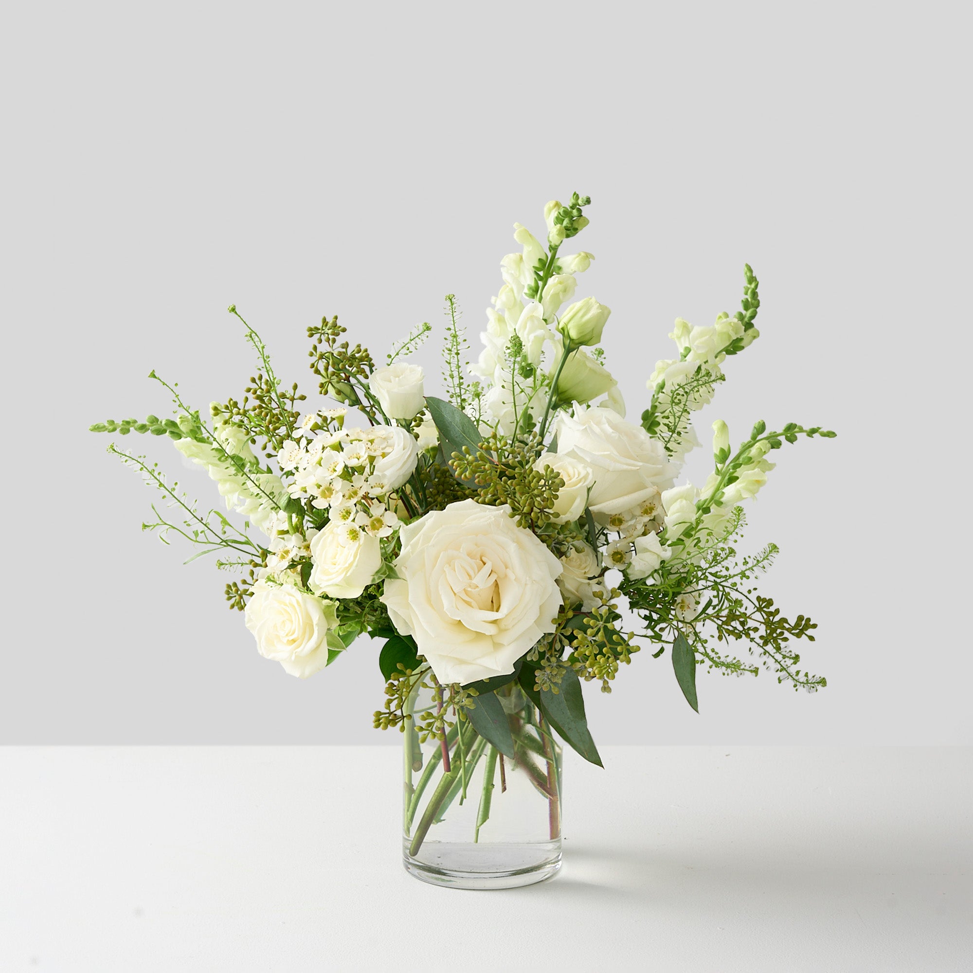 elegant all white and green country garden vase arrangement which features hydrangea, snapdragons, Playa Blanca roses, lisianthus, seeded eucalyptus, and white spray roses.