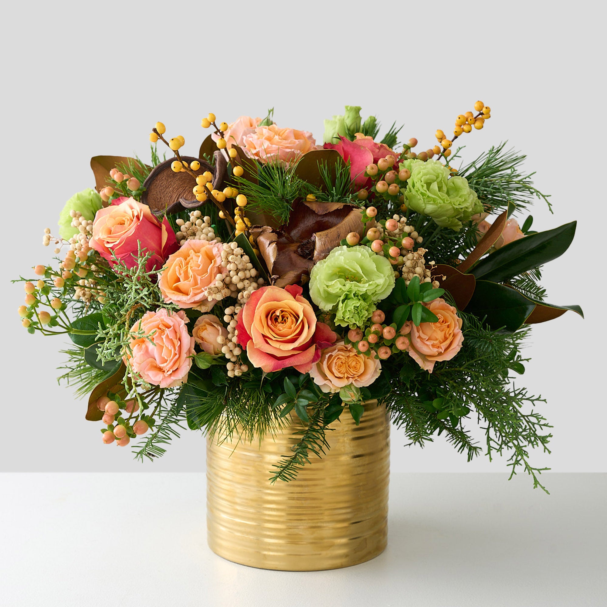 large arrangement of peach roses, hypericum, green double Lisianthus, magnolia leaves, cedar, palm pods and white pine in a gold tin pot.