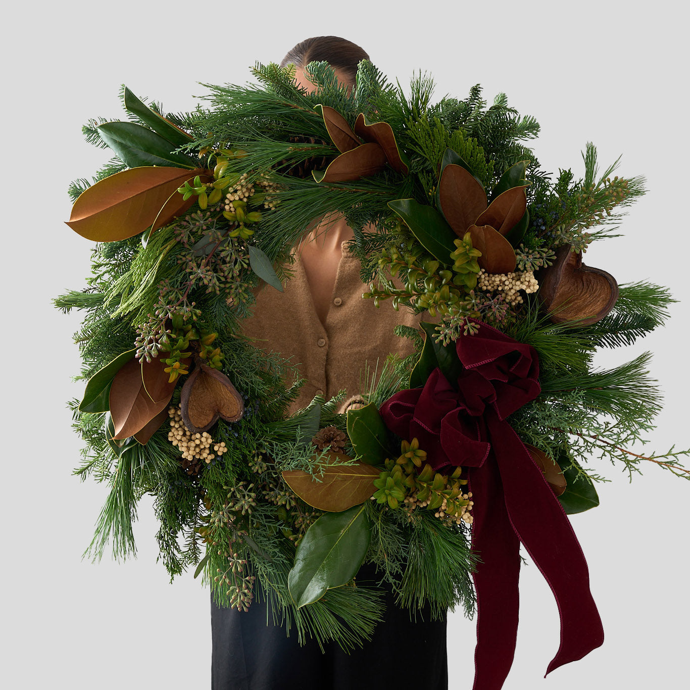 Fresh Christmas wreath with pepper berries, badam pods, magnolia leaves, cedar, fir and pine greens with a burgundy bow