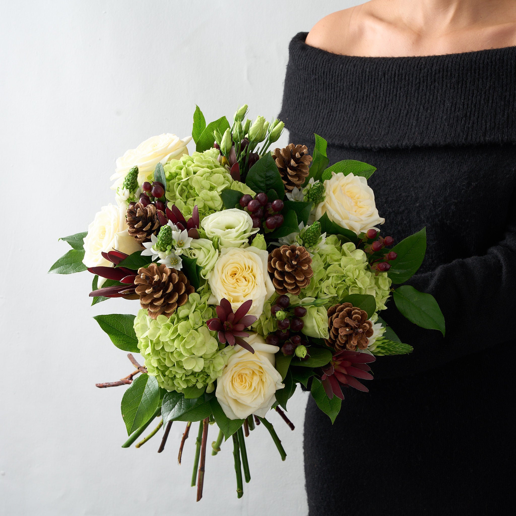 woman in black dress holding a bouquet of white roses, lisianthus, star of Bethlehem, pine cones and green hydrengea