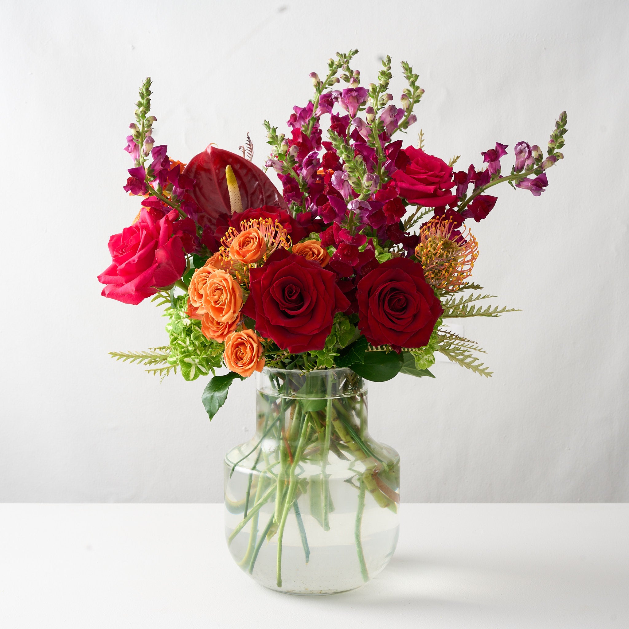 floral arrangement featuring deep red roses, vibrant orange hues, and striking red anthuriums in a bold and luxurious display.