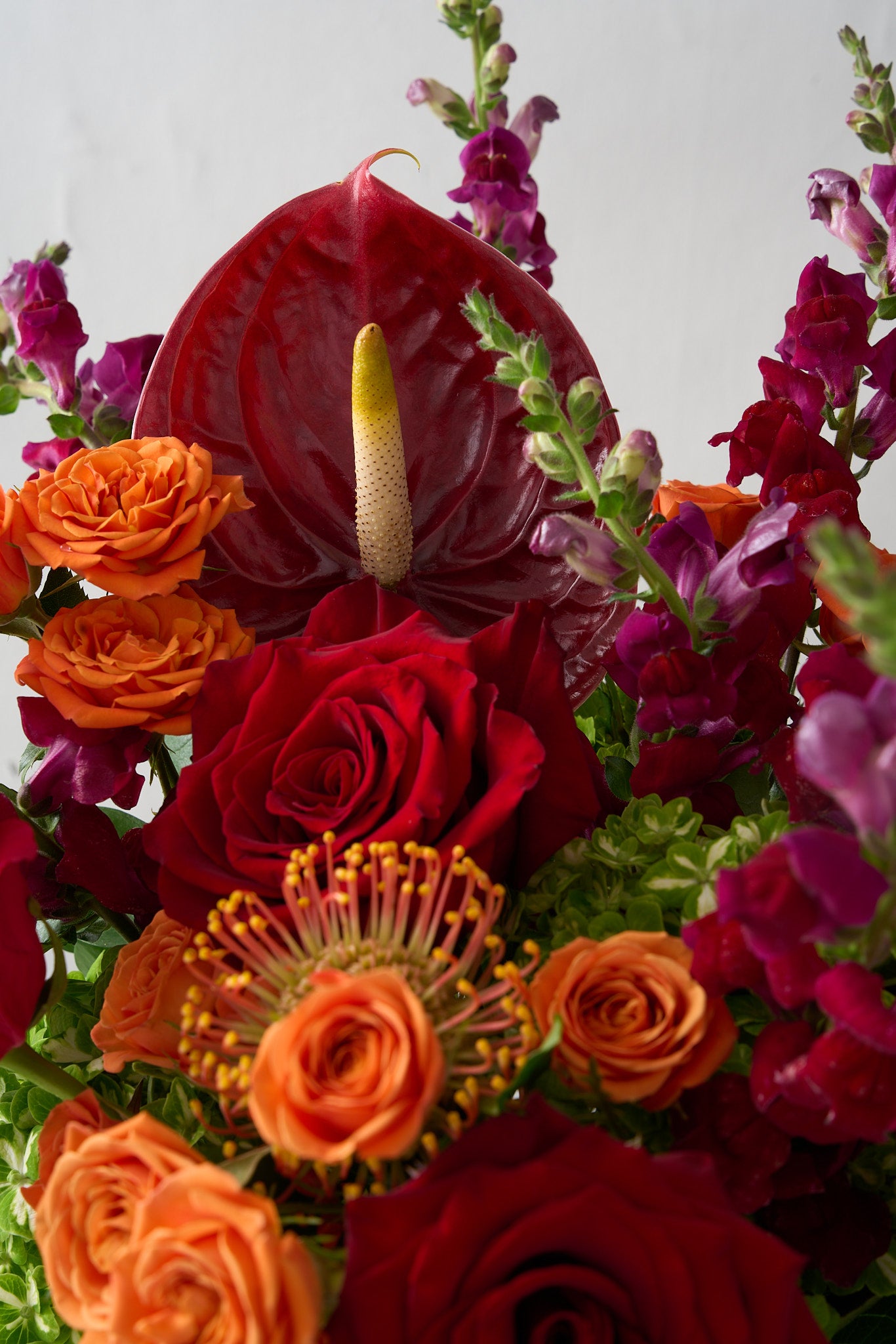 up close shot of a floral arrangement featuring deep red roses, vibrant orange hues, and striking red anthuriums in a bold and luxurious display.