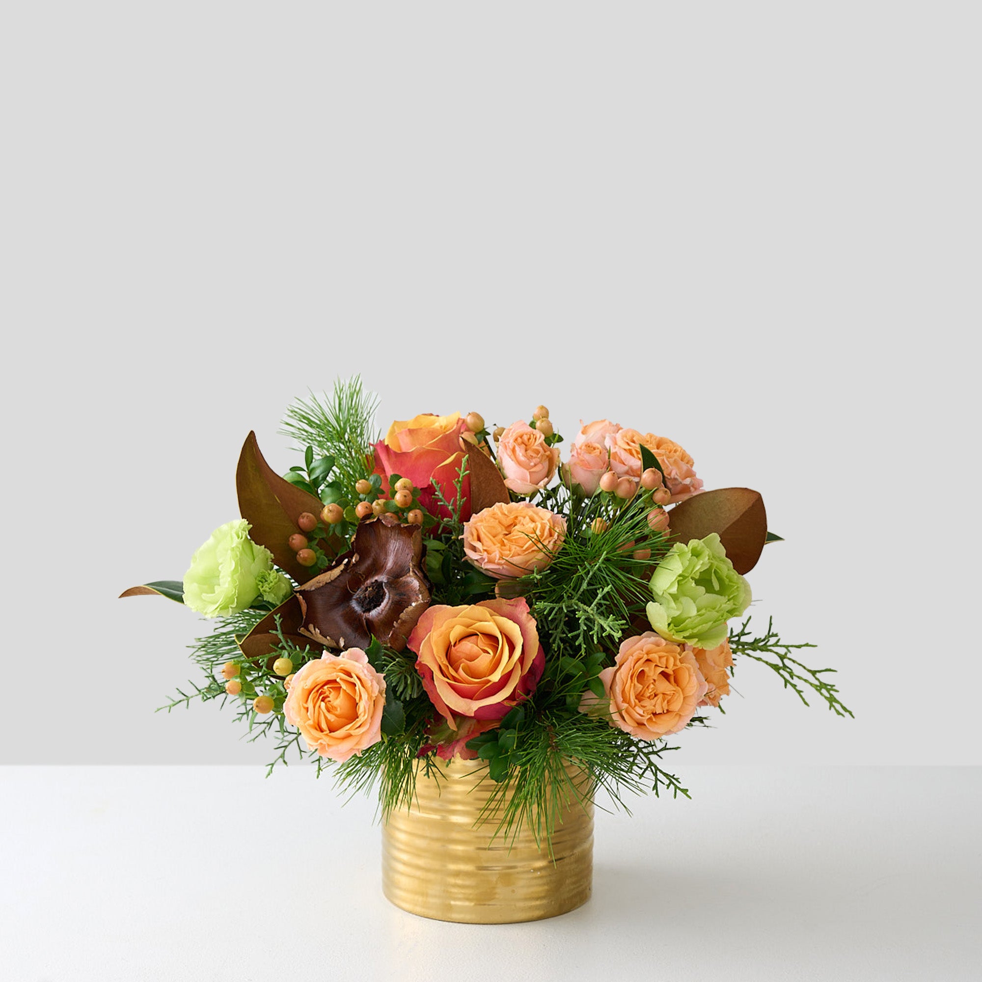 Peach roses, hypericum, green double Lisianthus, magnolia leaves, cedar and pine in a gold tin pot.