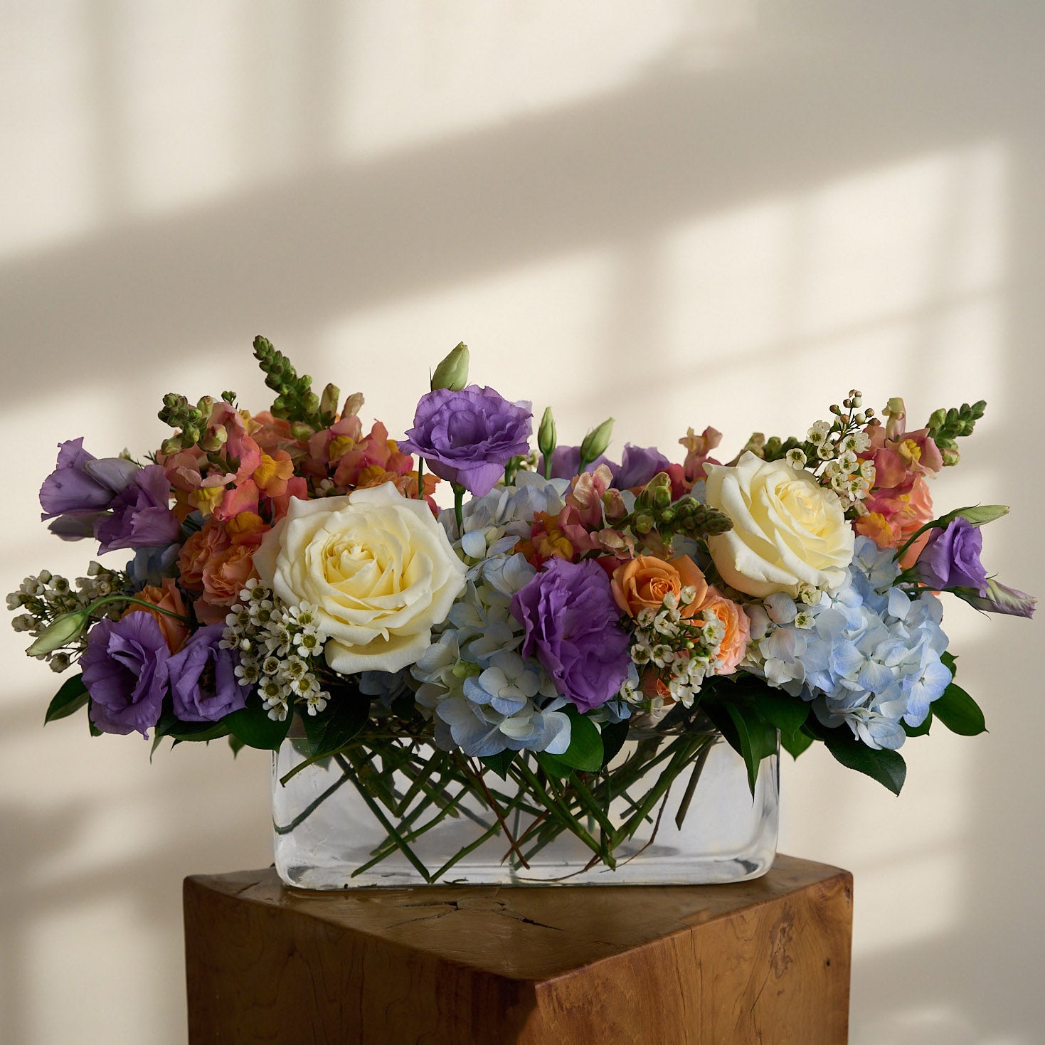 Colorful Easter floral centerpiece arrangement in a glass vase on a wooden side table with a neutral background