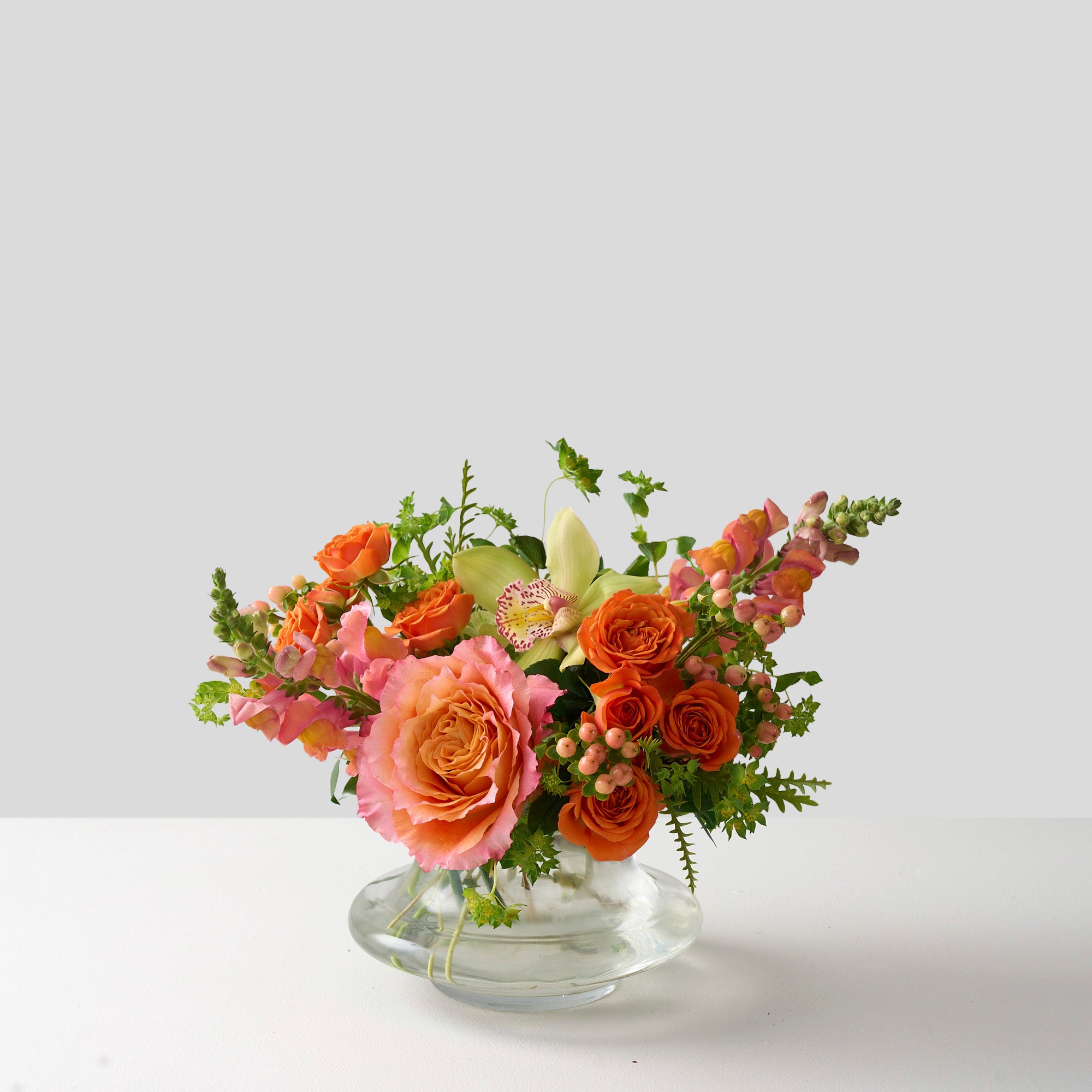 ellie flower arrangement in clear glass vase with orange spray roses, peach snapdragons, green cymbidium orchid and Bupleurum